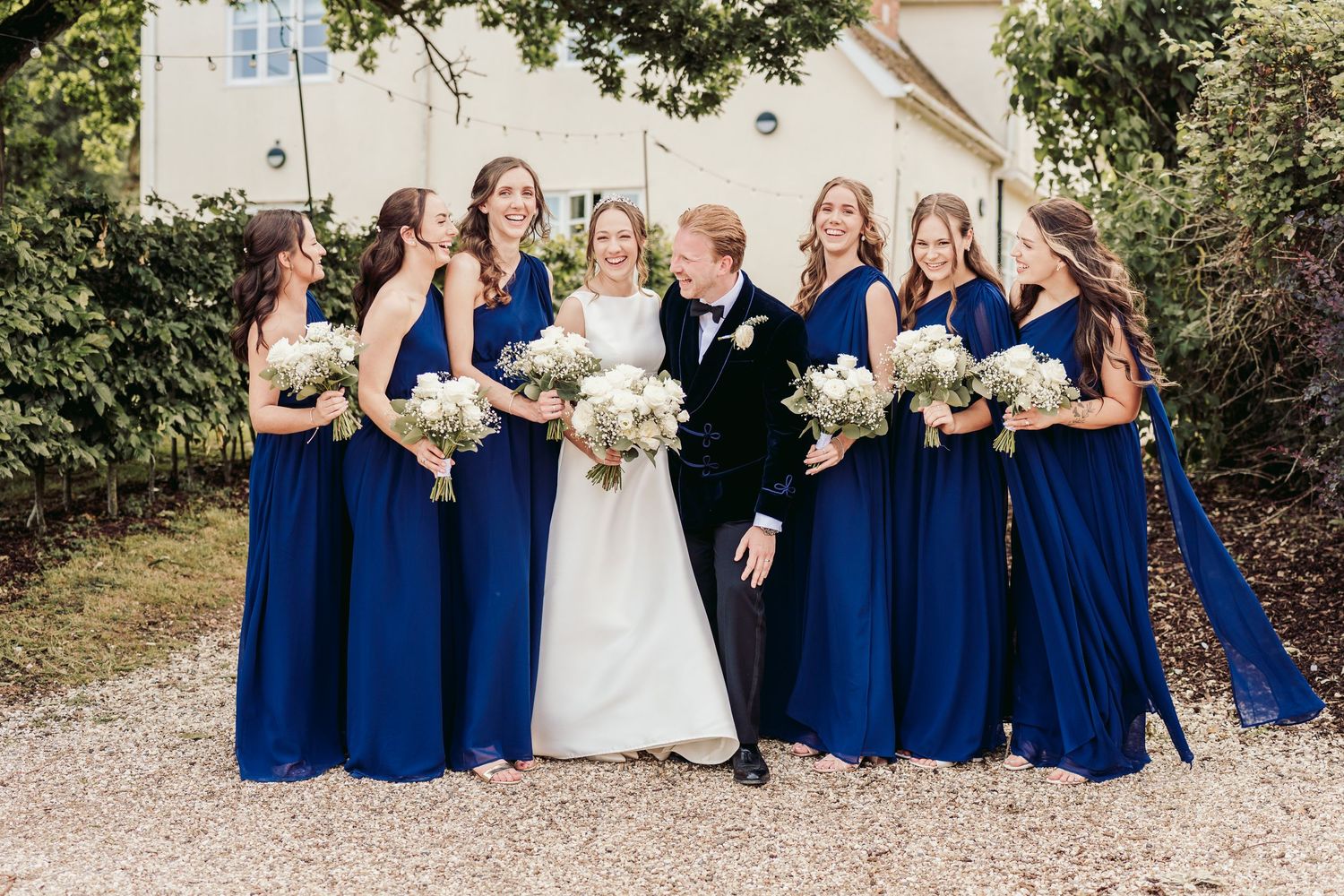 Wedding party in navy blue dresses and white gown pose together outdoors in a candid sequence of celebratory shots.