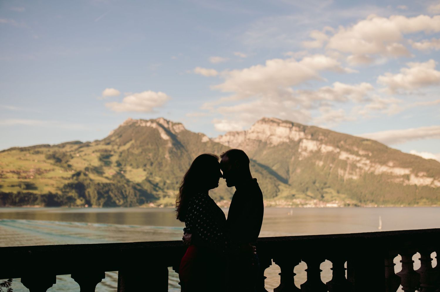 A silhouetted couple shares a romantic moment against a backdrop of mountains and lake during sunset.Spiez switzerland destination wedding
