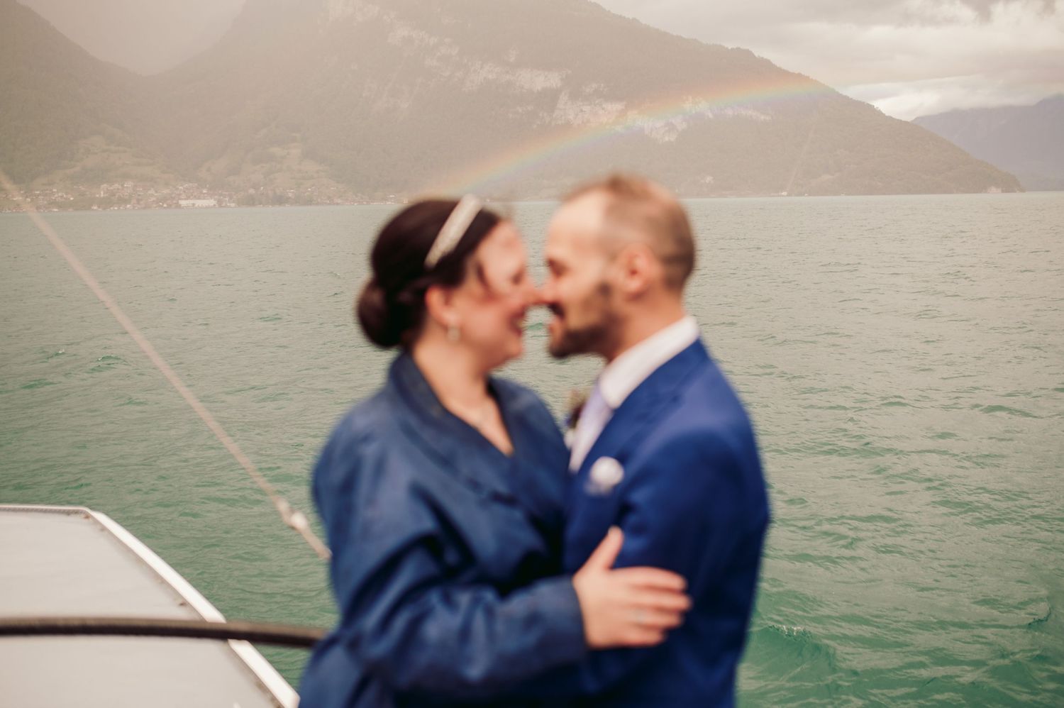 A romantic couple embraces on a boat with misty mountains and a lake in the background.Spiez switzerland destination wedding