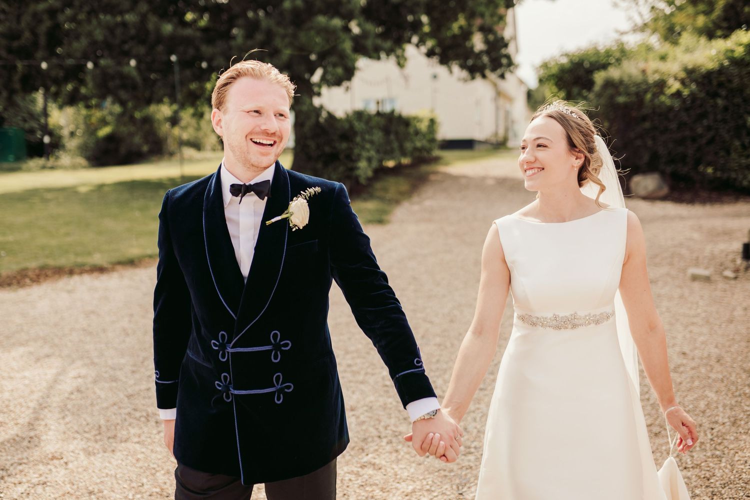 A joyful wedding couple shares candid moments together while walking through a sunlit outdoor garden setting.