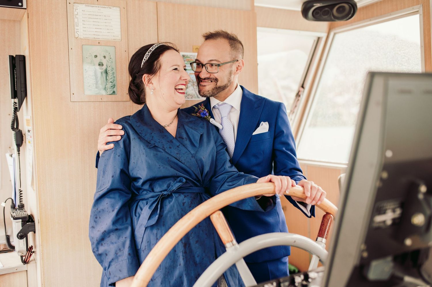 Two people share a joyful moment at the wheel of a boat, with one wearing a navy robe and the other in a blue suit.Spiez switzerland
