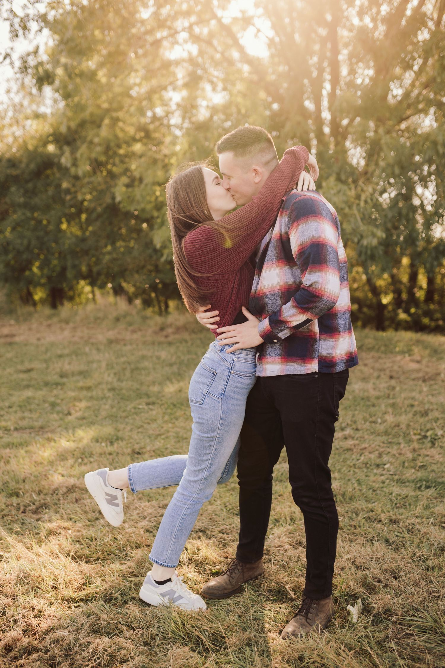 A romantic couple embraces in a sunlit field during golden hour.