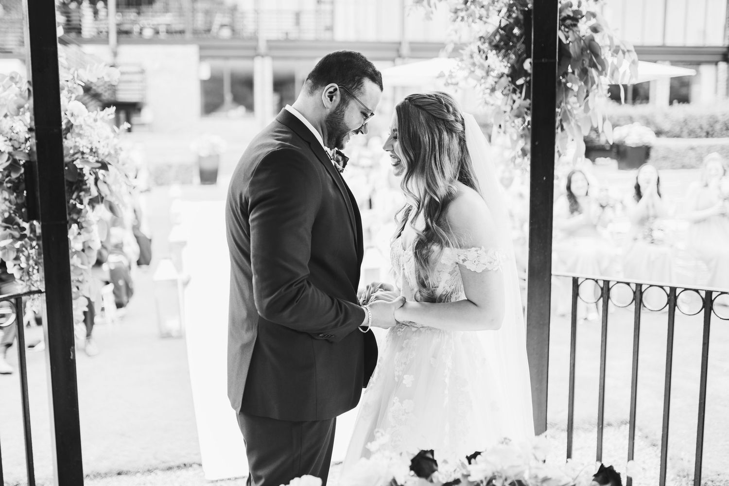 A black and white photograph of a couple in wedding attire sharing an intimate moment on a balcony.