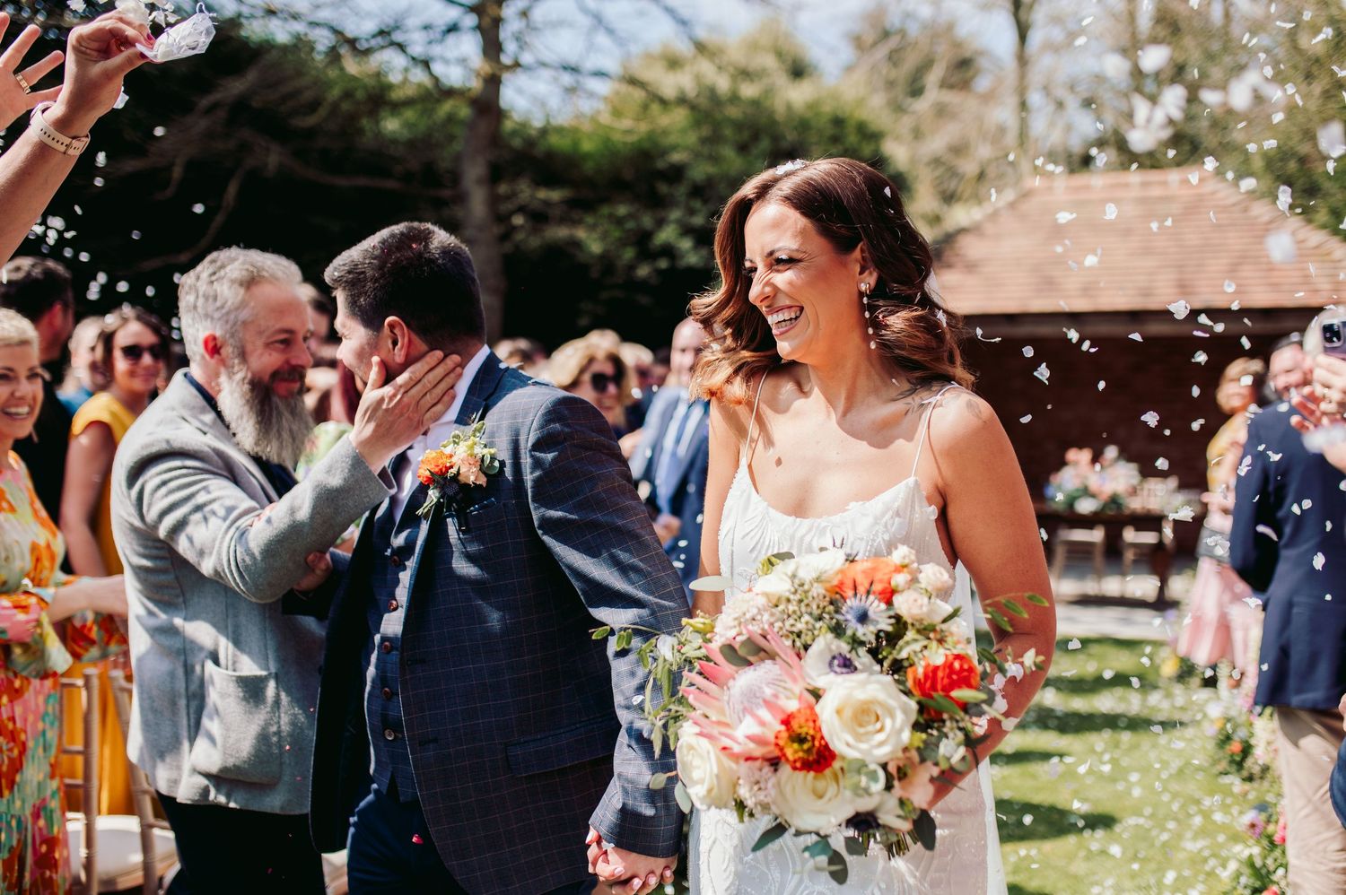 Wedding party celebrating outdoors with confetti and laughter on a sunny day.
