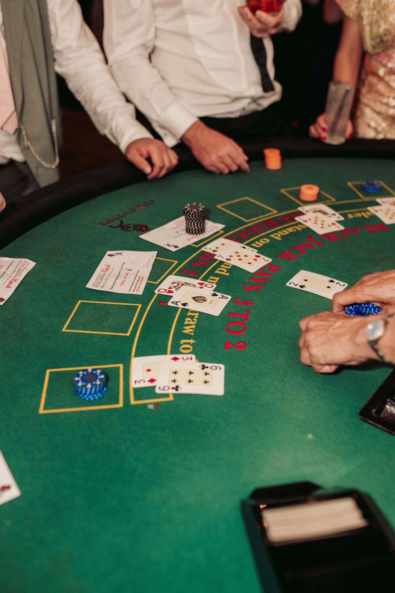 Overhead view of a blackjack table at a casino showing cards, chips and players' hands during an active game.