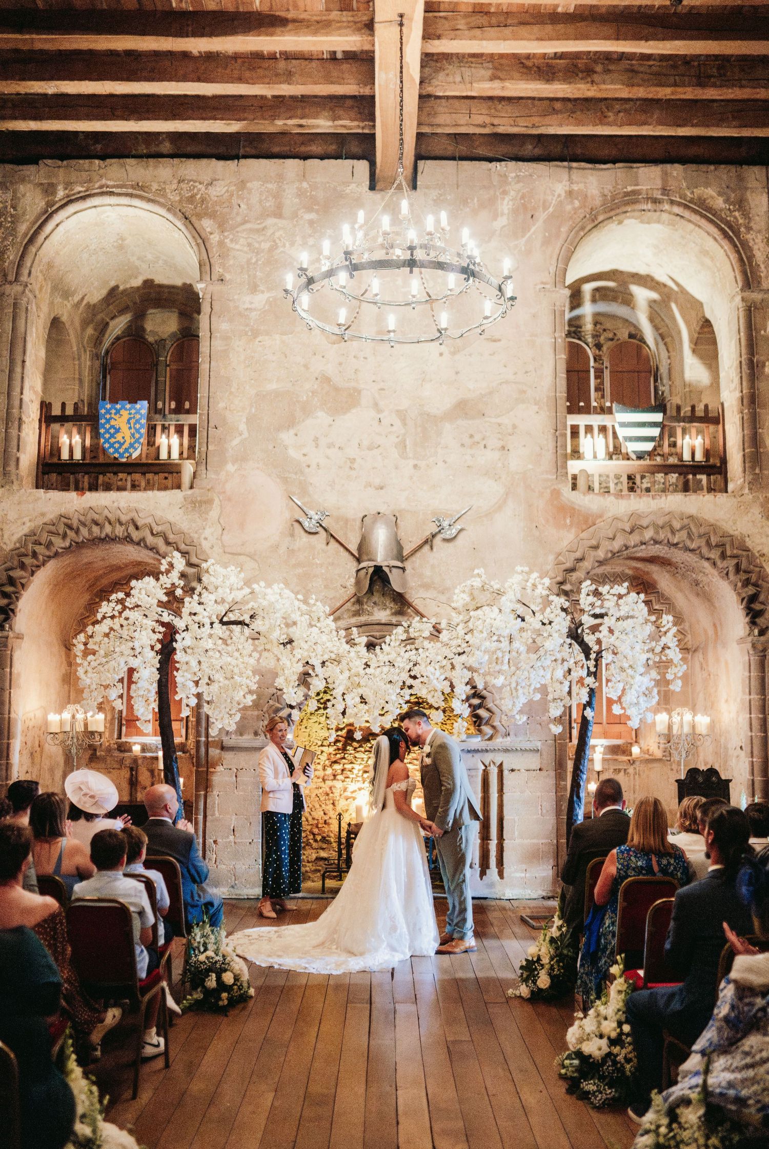 Rustic barn wedding ceremony with chandeliers and white floral arrangements.
