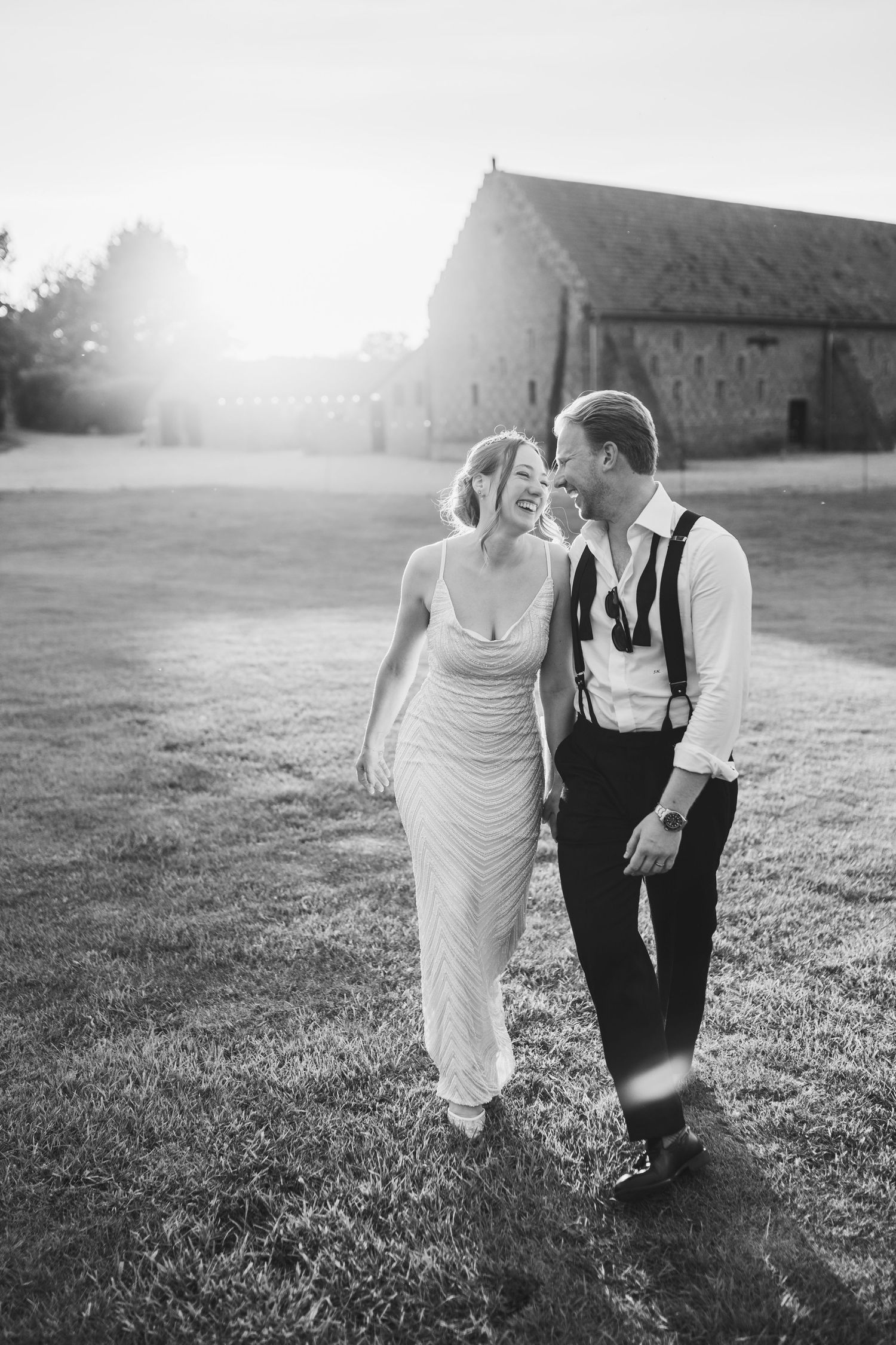 A couple walks hand in hand across a sunlit field in black and white vintage-style wedding photography.