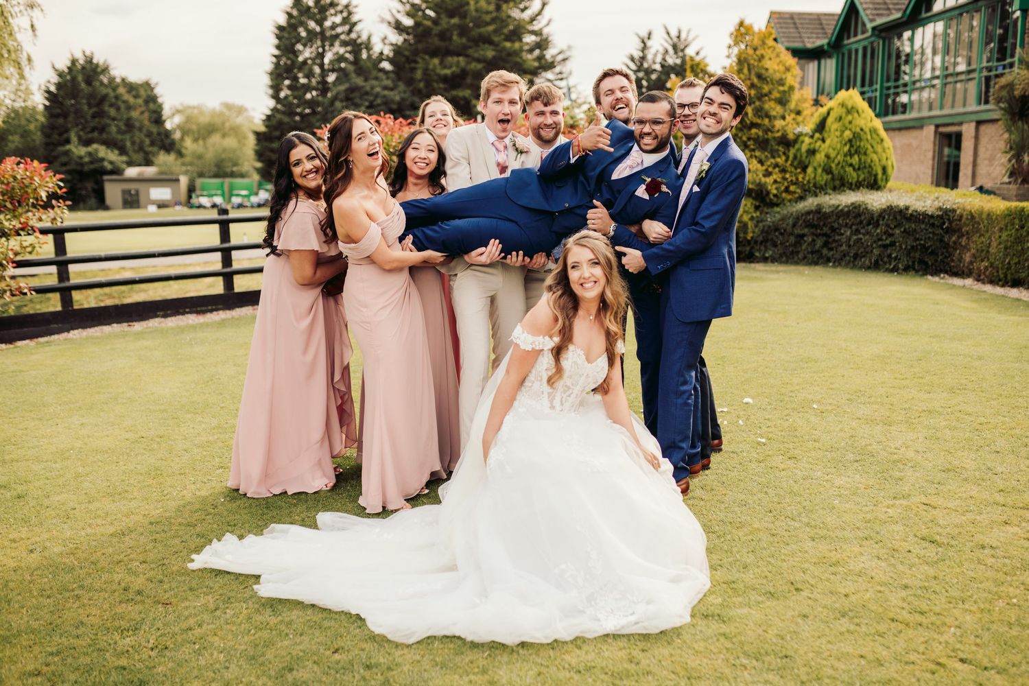 Wedding party poses playfully on a green lawn in front of a country estate on an autumn day.