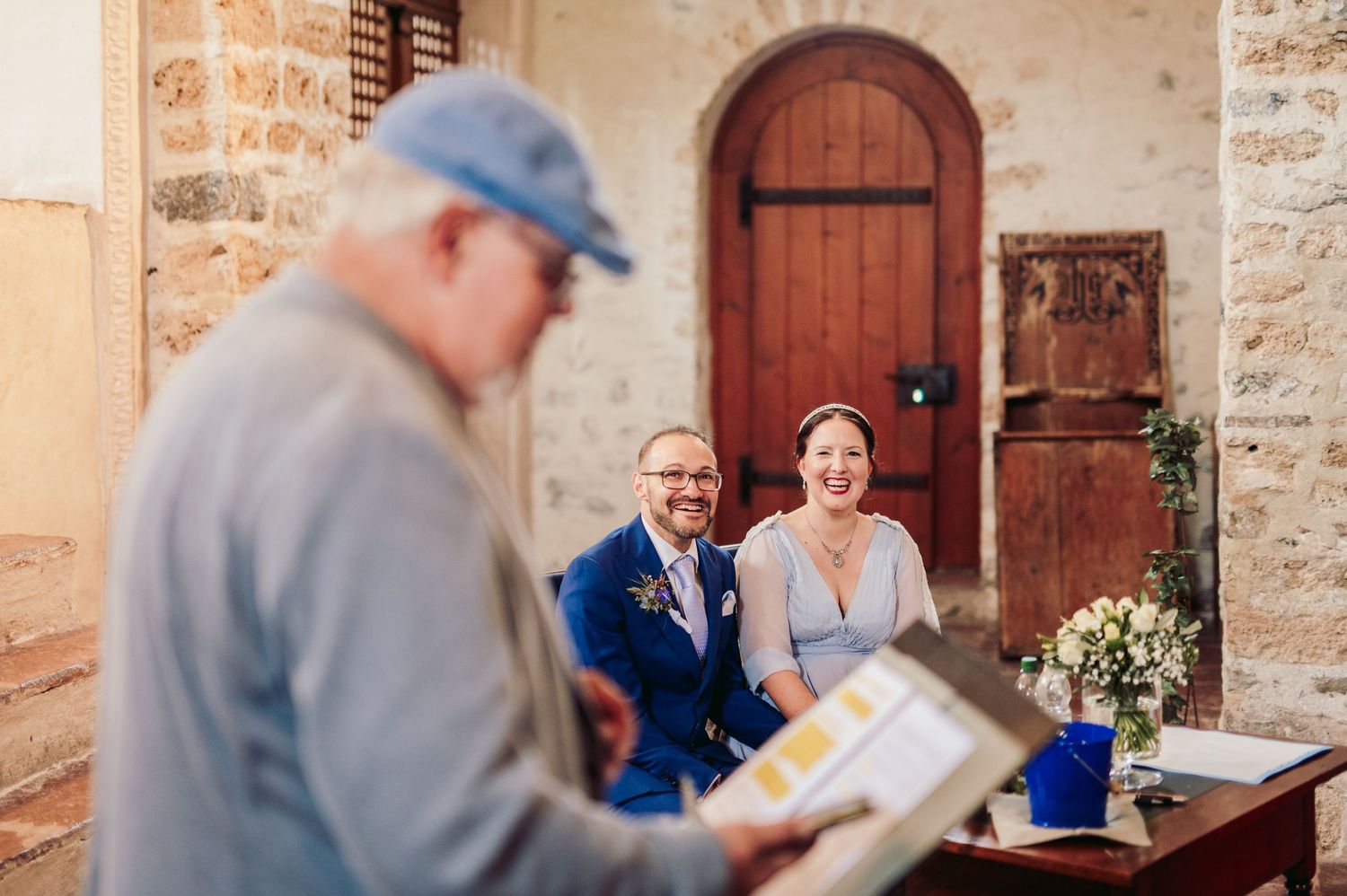 Wedding guests seated at rustic stone venue while someone in blue cap reviews a document. Spiez switzerland destination wedding