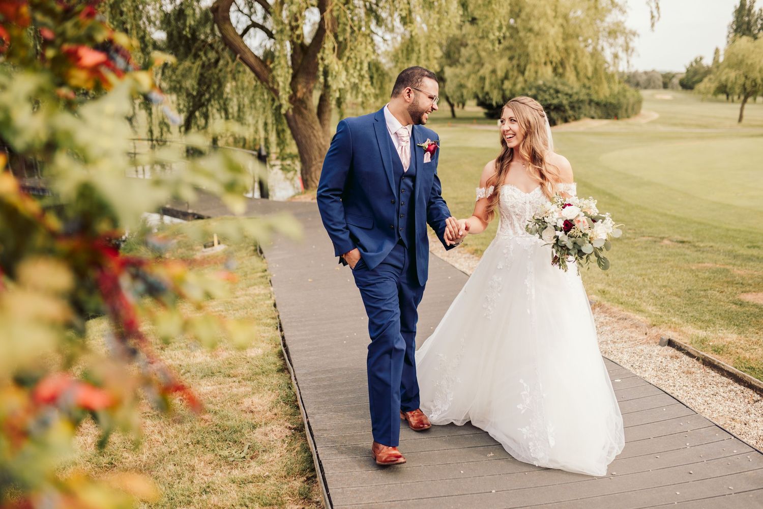 A couple on their wedding day share a joyful moment while walking together on a garden pathway.
