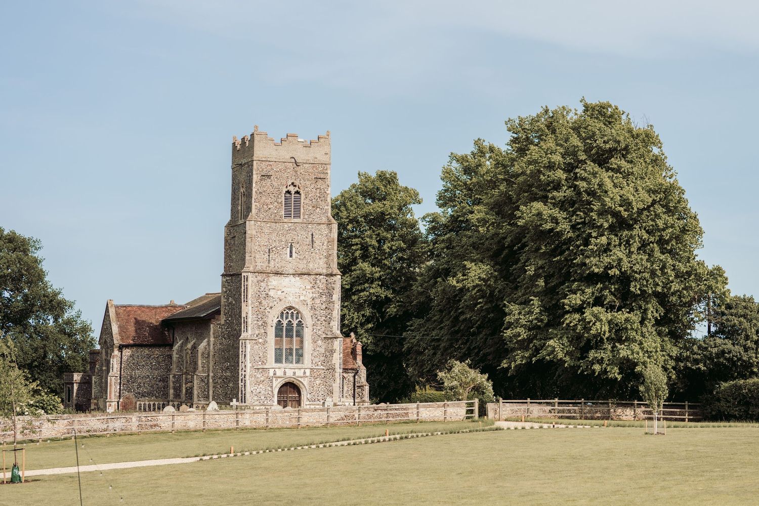 A panoramic view of an ancient stone church with a tower surrounded by green trees and a grassy landscape.