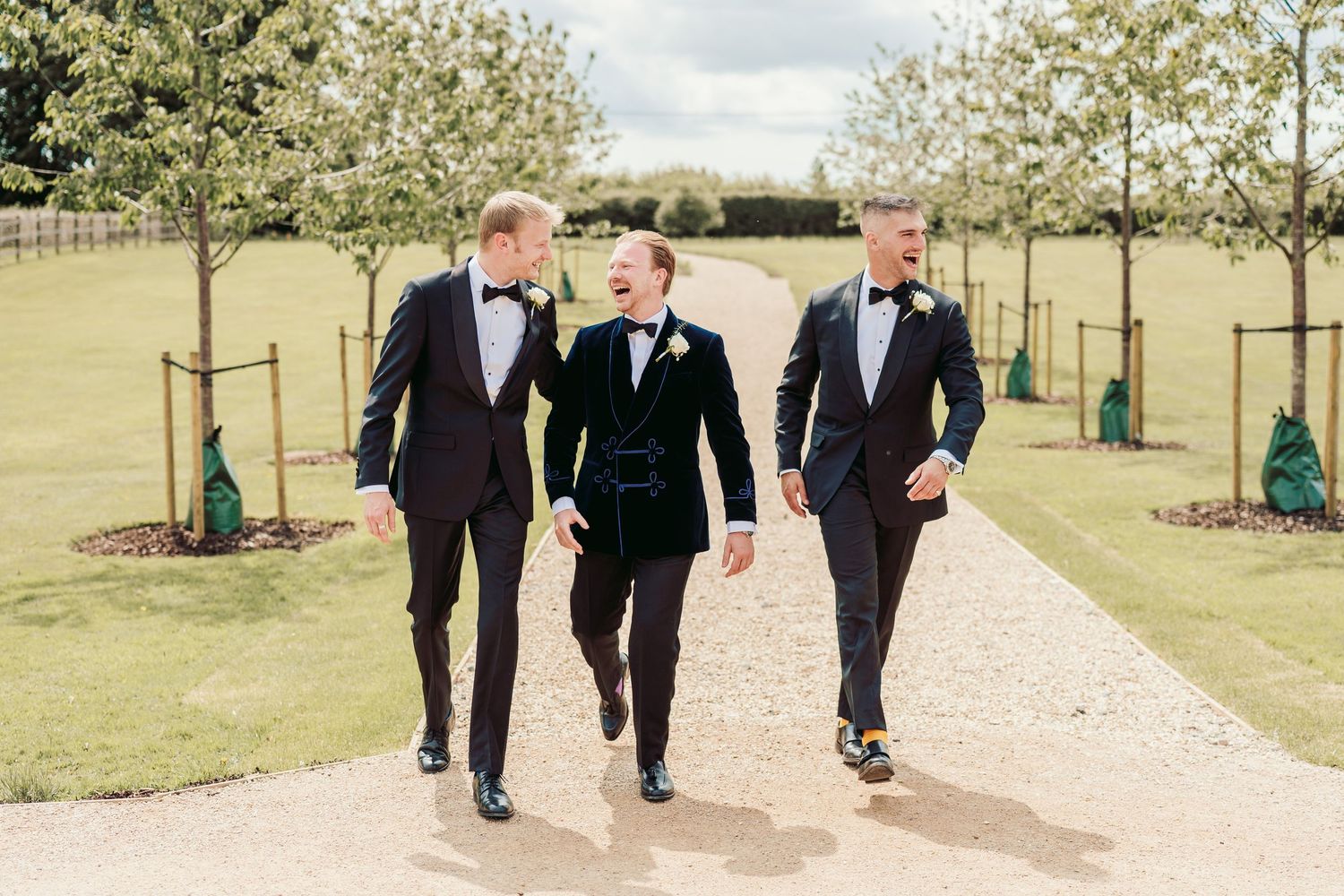 Wedding party members in formal black attire walk along a scenic outdoor path during a spring celebration.