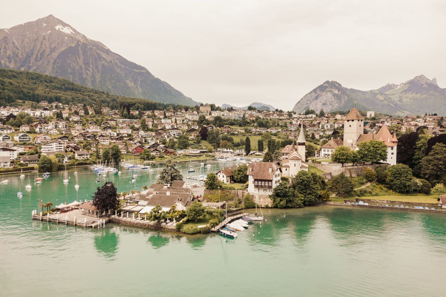 Aerial view of a lakeside town in Switzerland with turquoise waters and mountain peaks in the background.Spiez switzerland destination