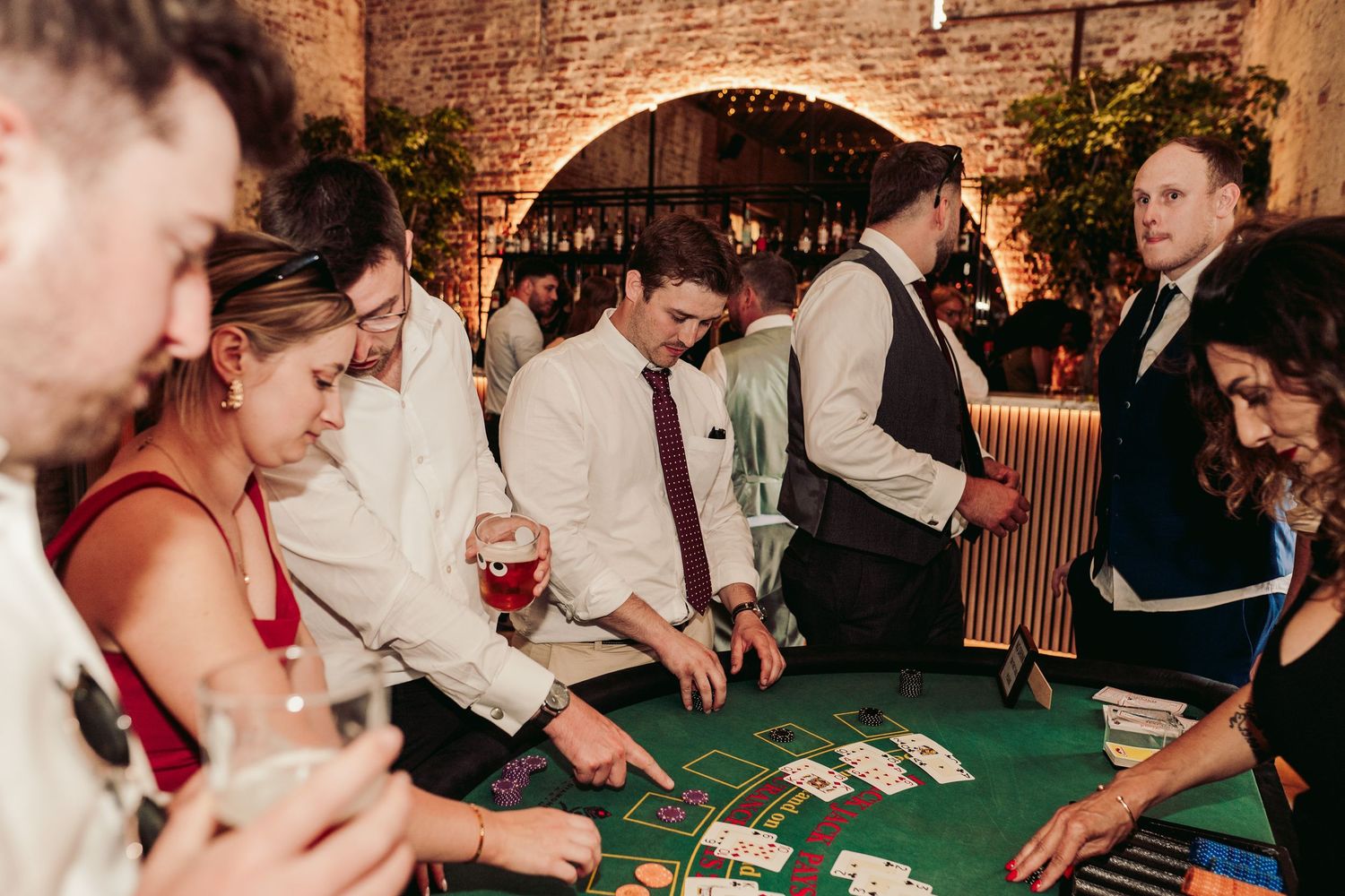 People gather around casino gaming tables at an event venue with players enjoying card games and roulette.