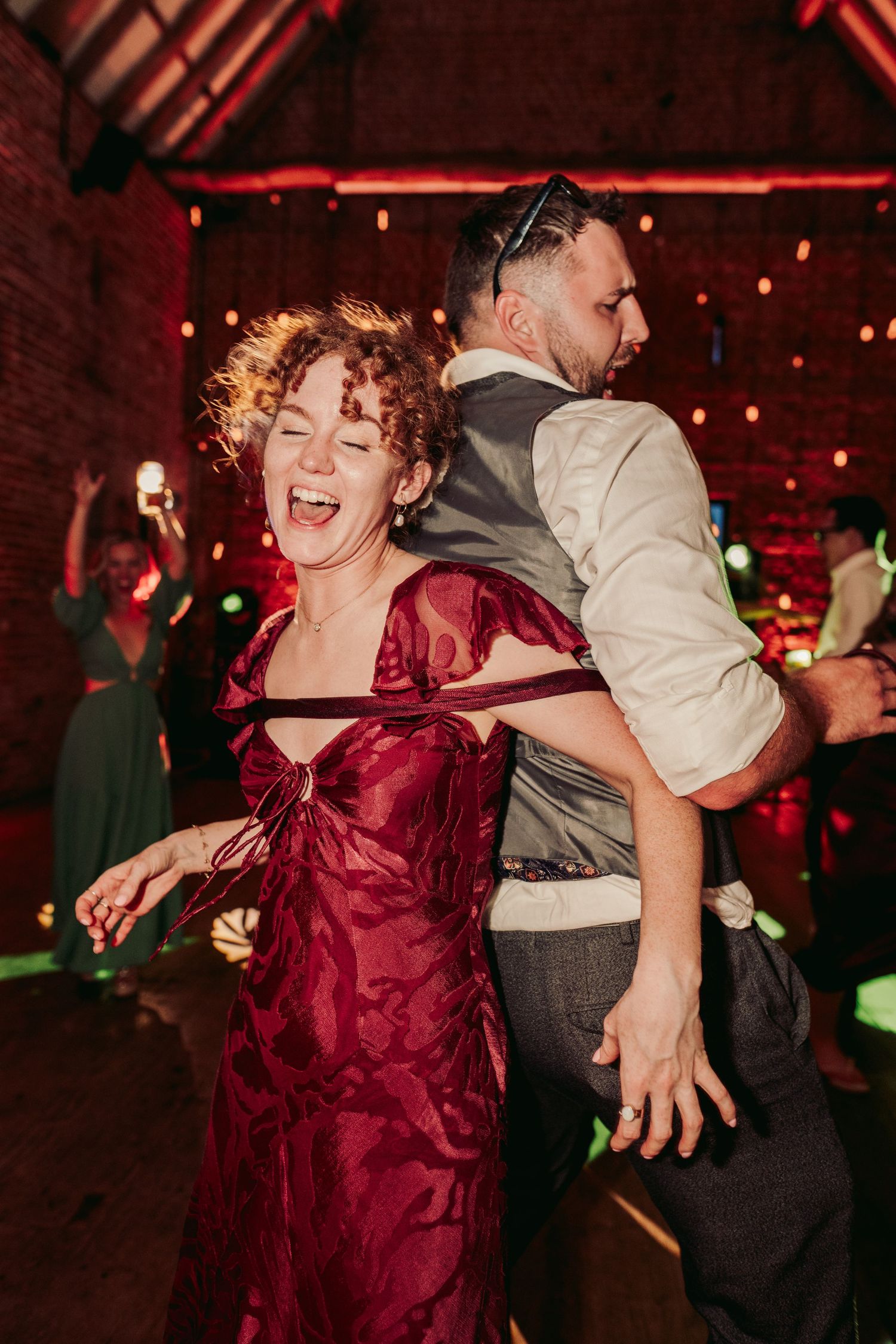 A person in a burgundy dress dances joyfully at a dimly lit event with red lighting.