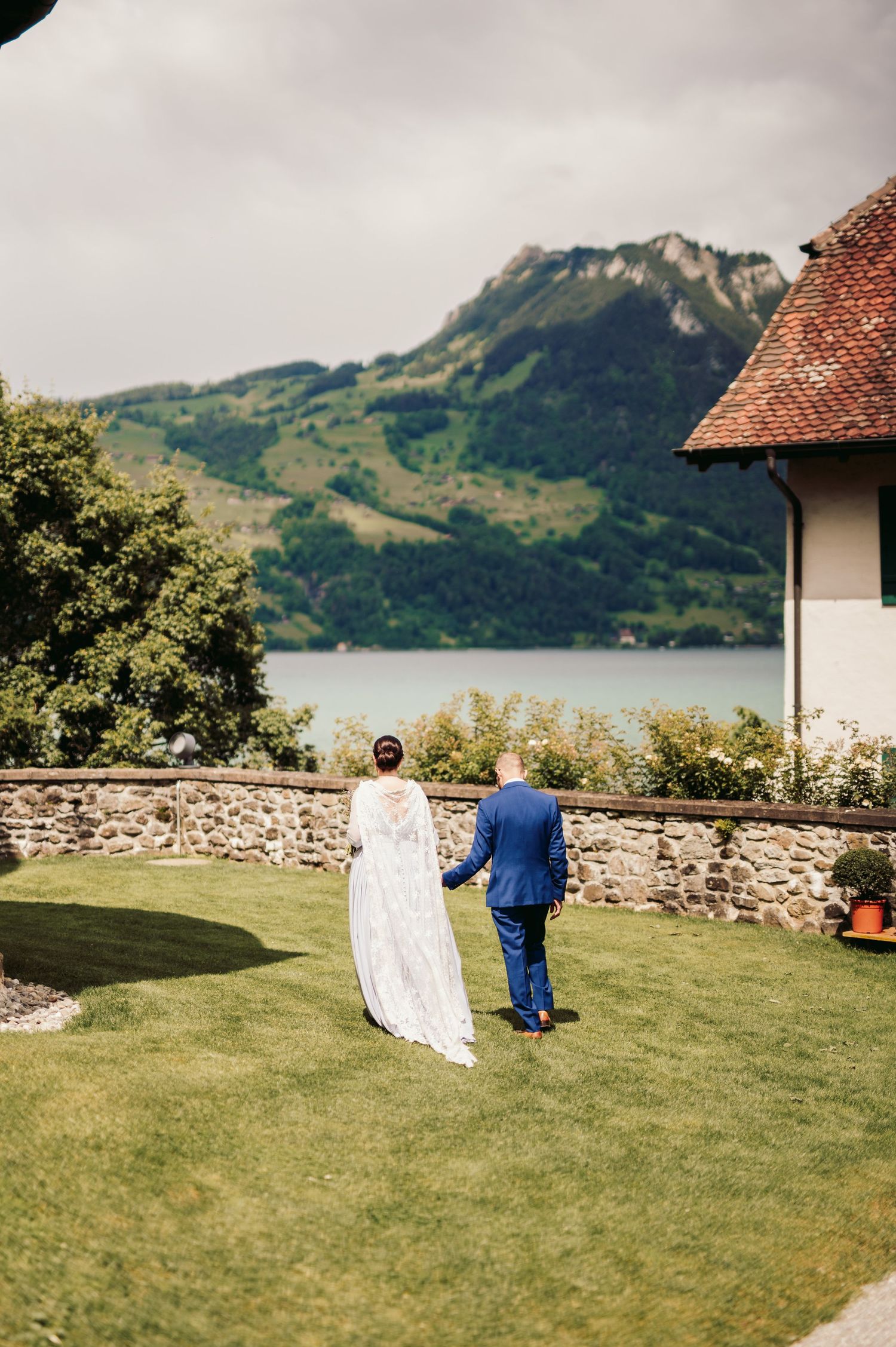 A couple walks on a scenic lawn overlooking a lake and mountains in Switzerland during a wedding celebration. Spiez switzerland destination