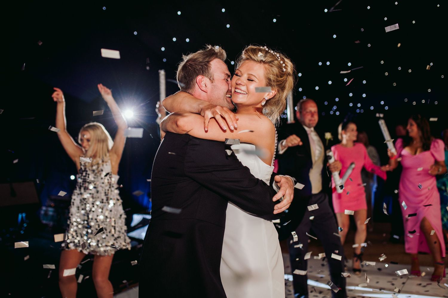 Couple shares romantic dance moment under falling confetti at wedding reception.