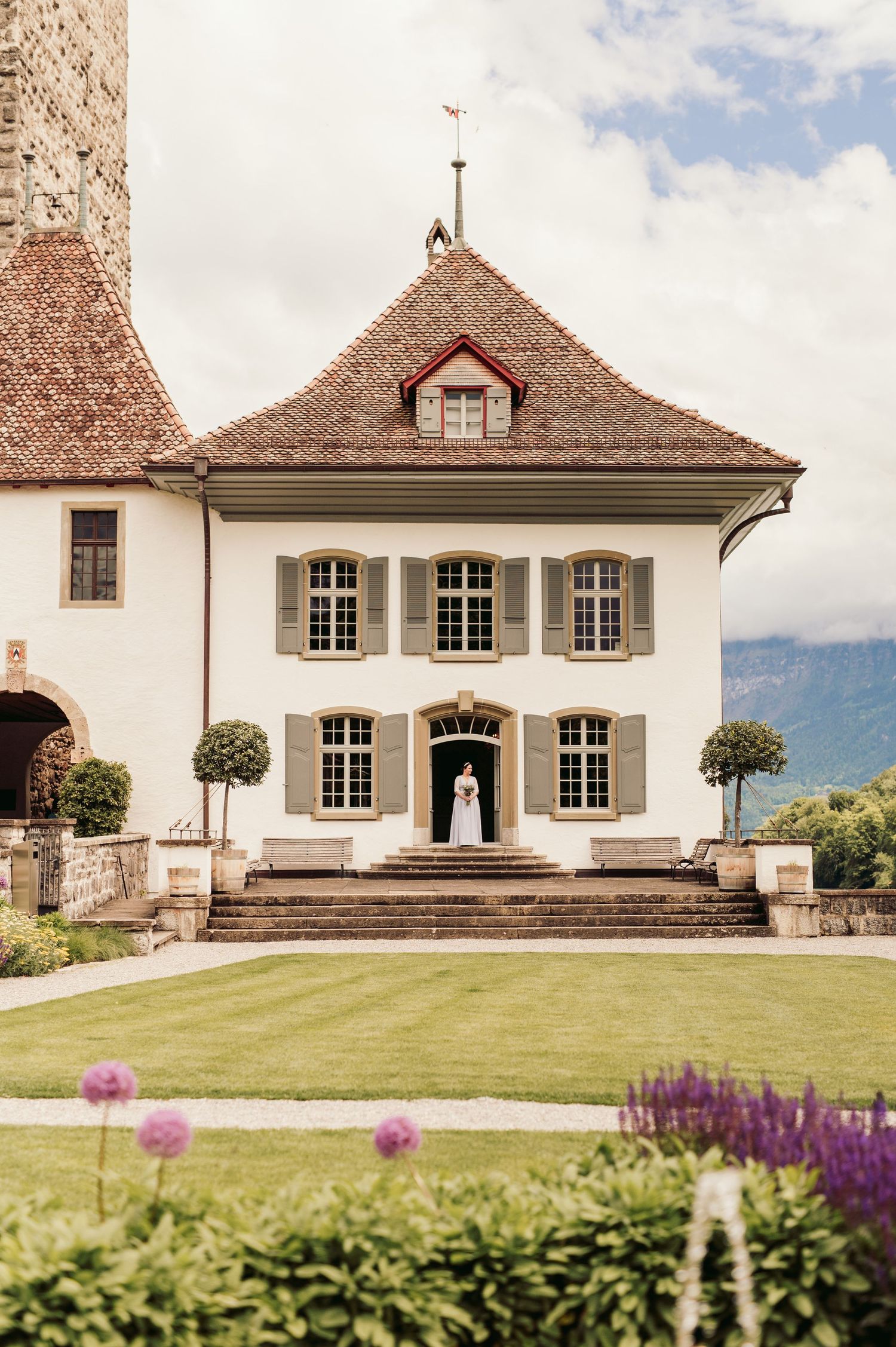 Elegant white Swiss mansion with symmetrical windows, pitched roof and manicured lawn with purple flowers in foreground. Spiez switzerland