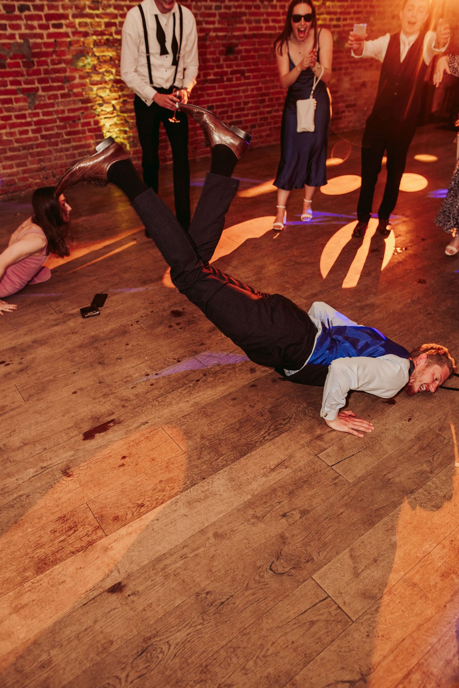 A sequence of dance moves showing someone performing a breakdancing windmill on a wooden floor against a brick wall.