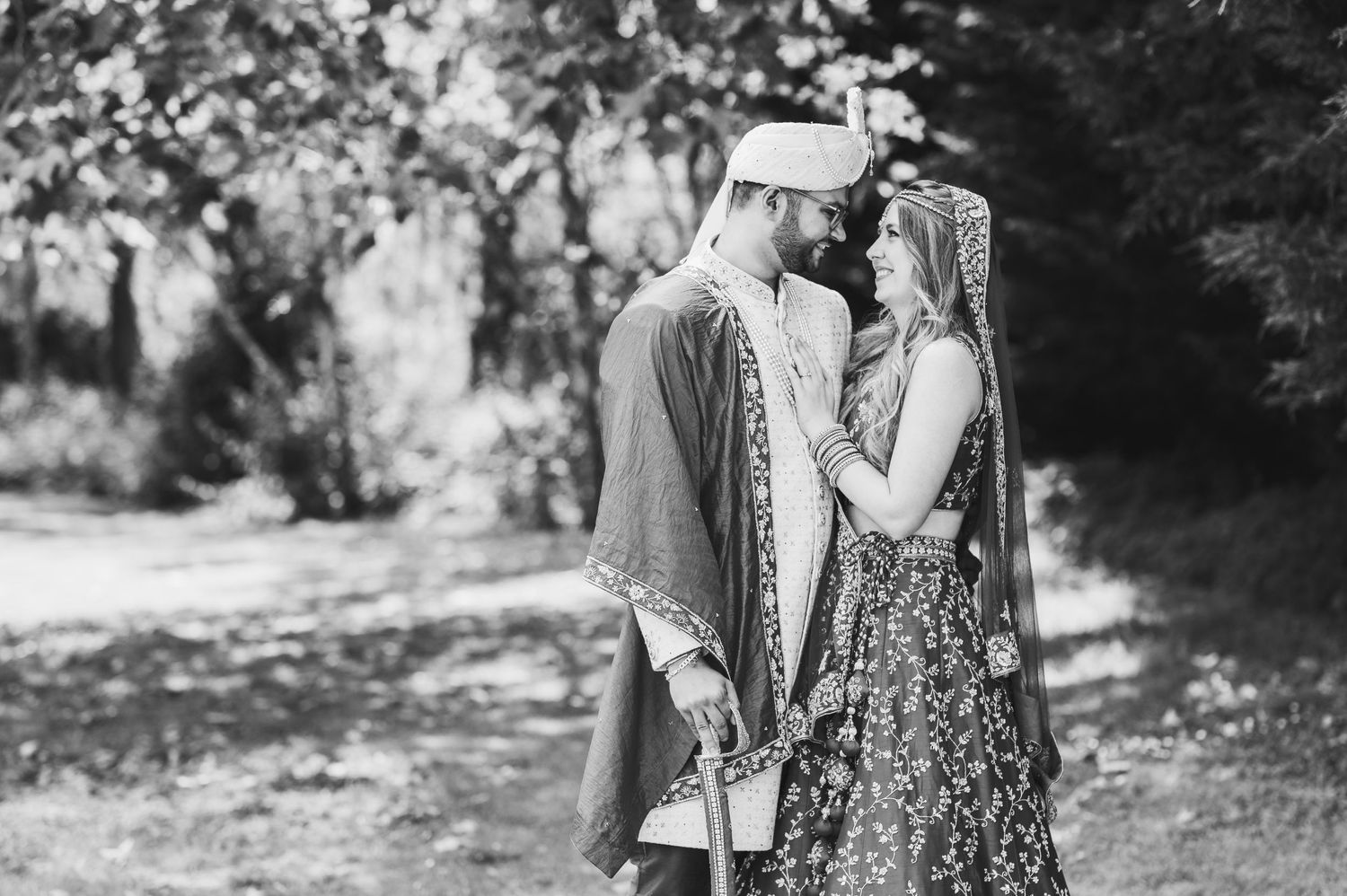 A romantic black and white portrait of a couple in vintage clothing embracing on a wooded path.