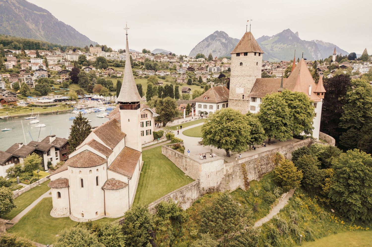 Aerial view of historic Spiez Castle and church overlooking Lake Thun in Switzerland with mountains in background.Spiez switzerland