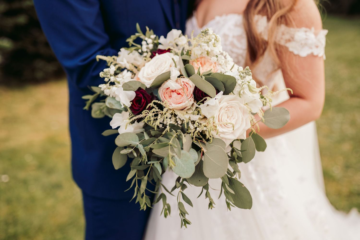 A romantic wedding bouquet featuring blush pink and white roses with cascading eucalyptus leaves against a navy suit.
