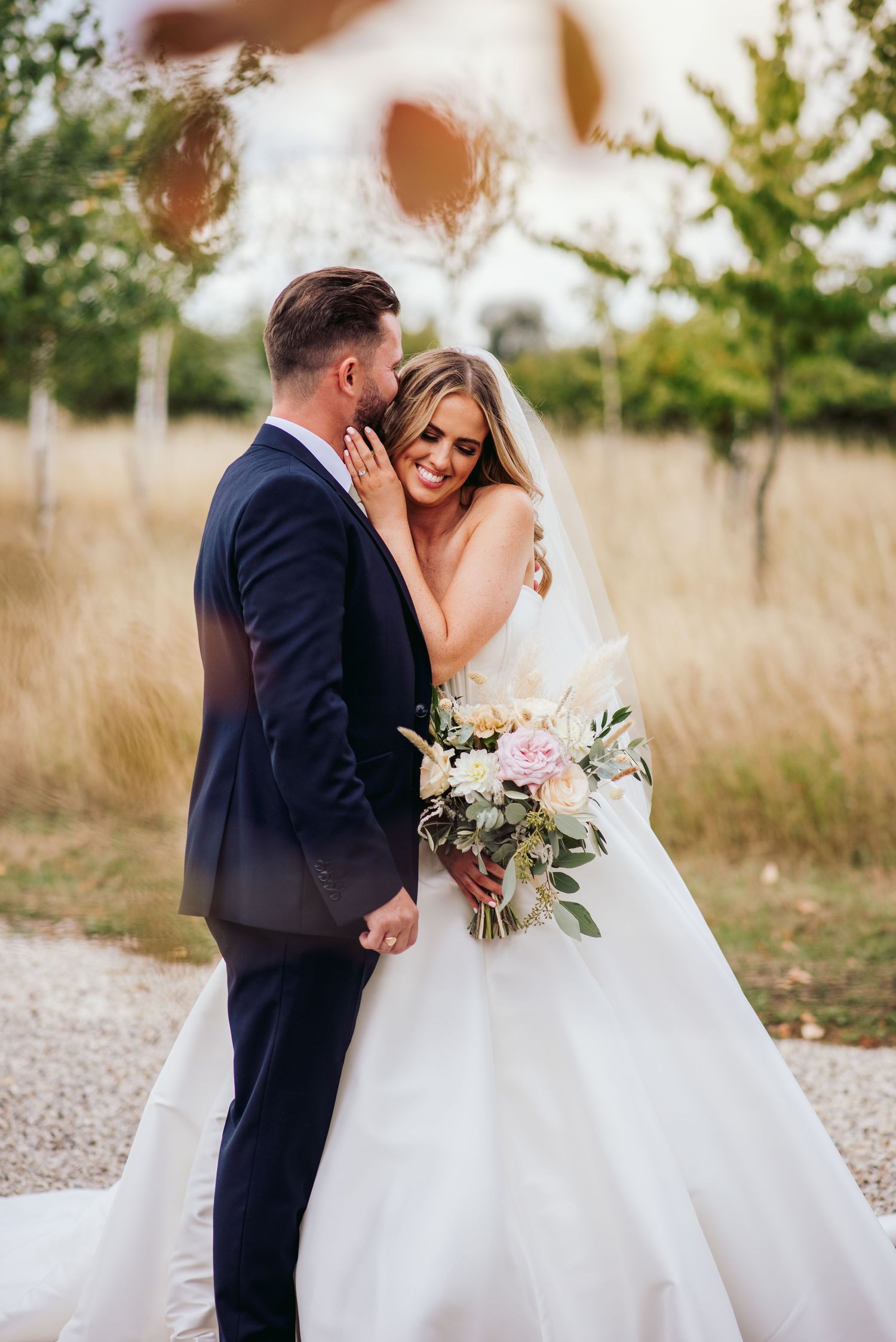 Romantic wedding portraits in natural field setting with soft lighting and floral bouquet.