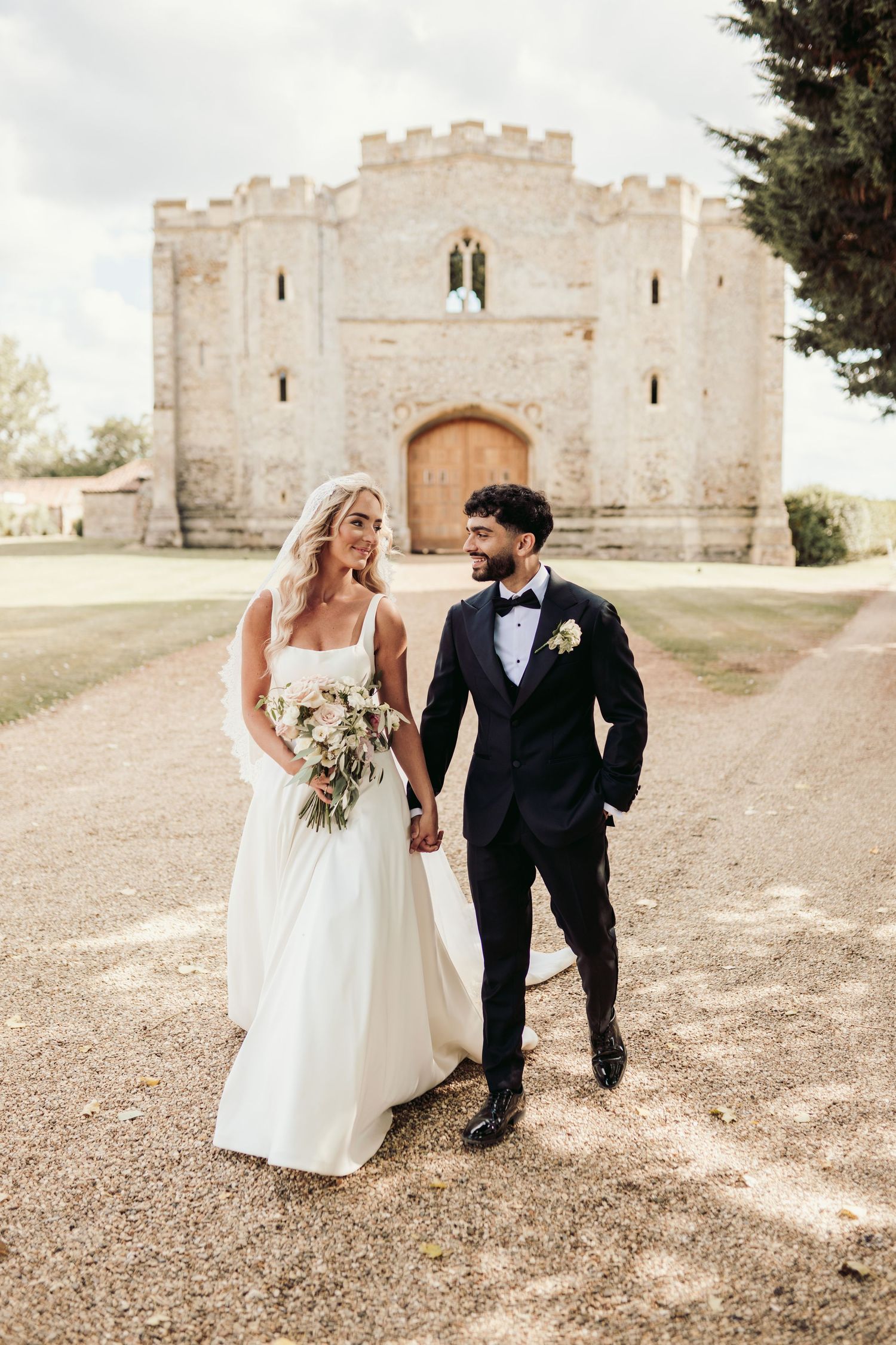 Couple poses playfully in front of a stone castle wall during their wedding photoshoot.