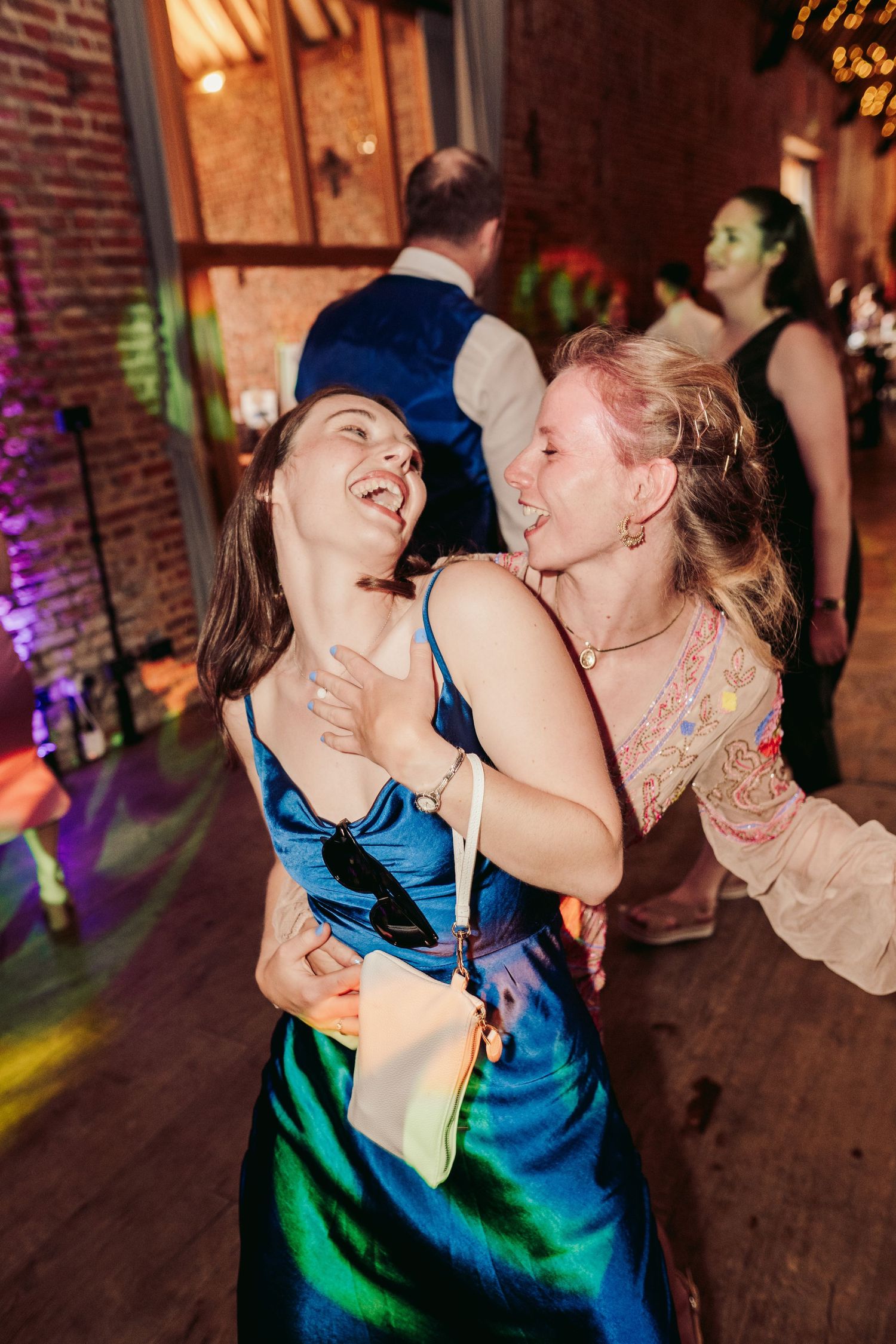 Couple sharing a joyful dance moment at a reception with colorful lighting and brick wall backdrop.