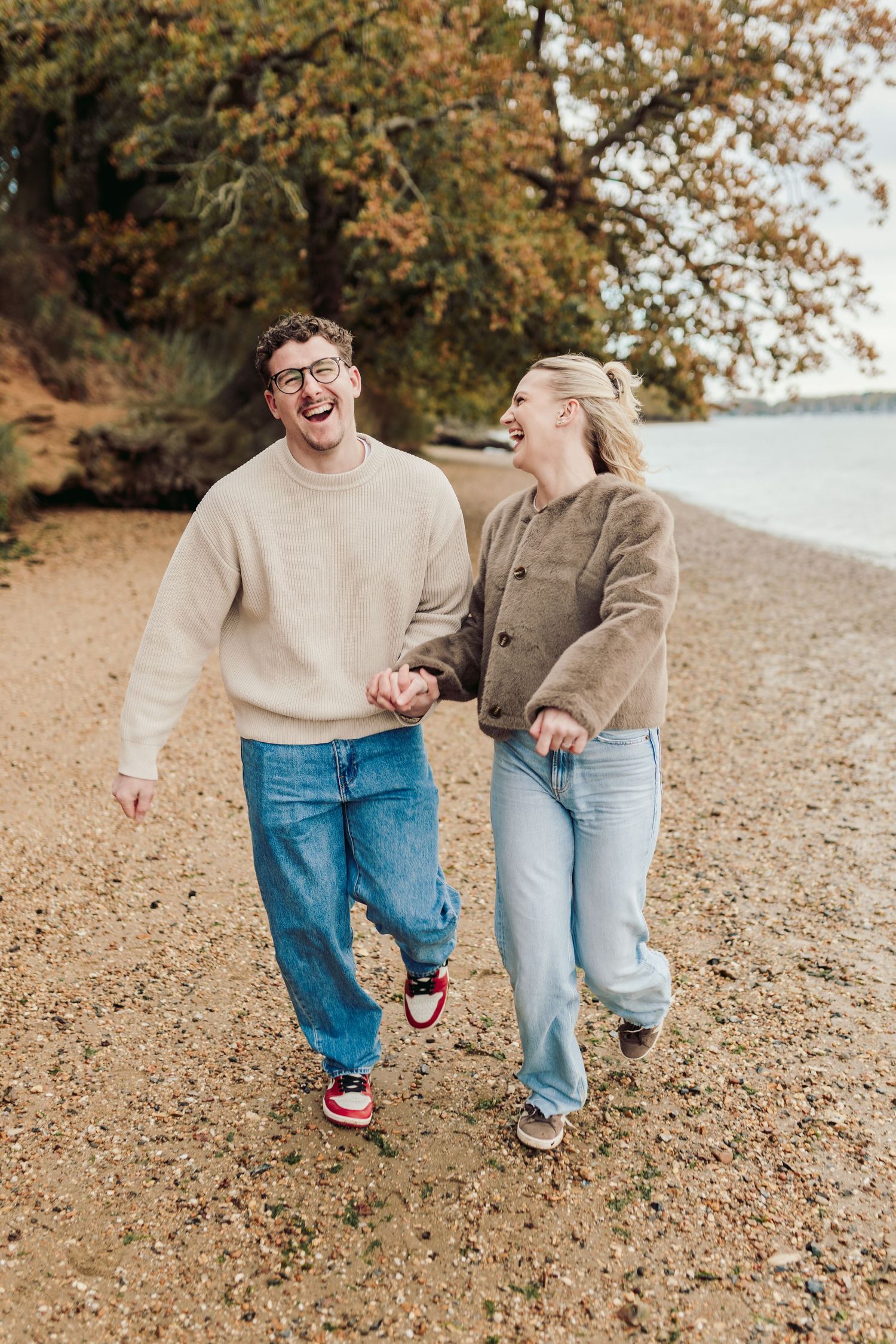 A joyful couple laughs while walking together on a beach path during autumn.
