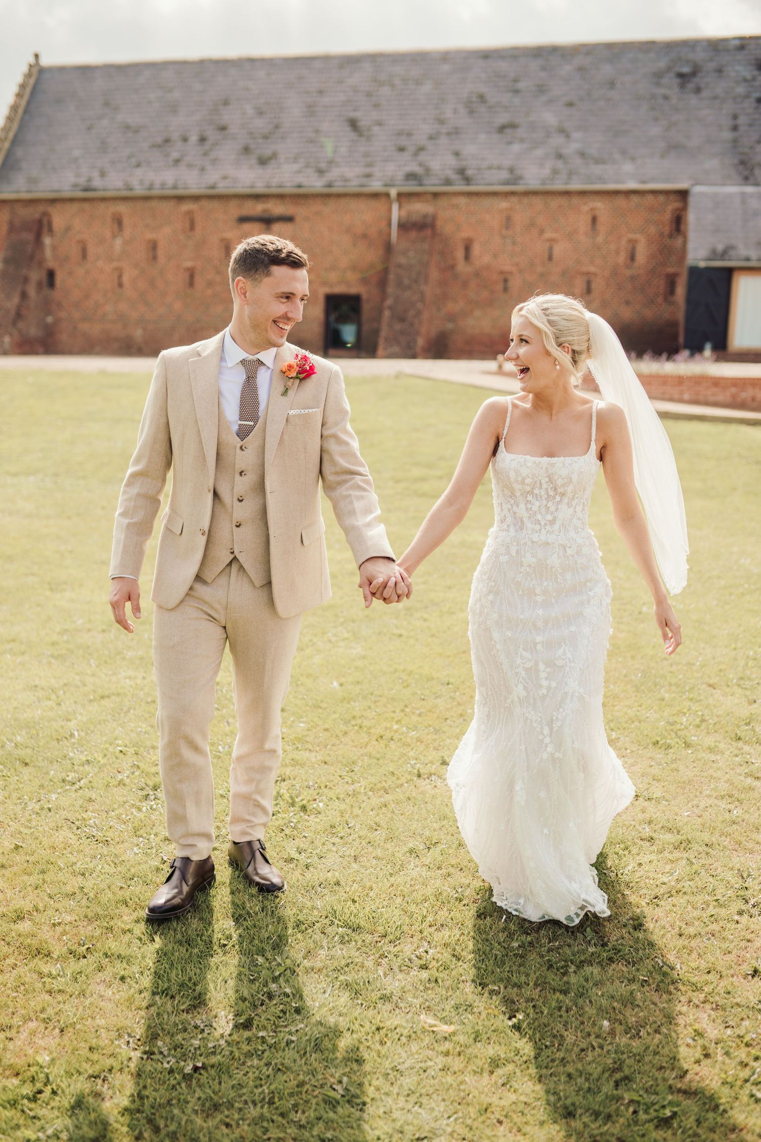 A couple strolls hand in hand across a grassy field in formal wedding attire.