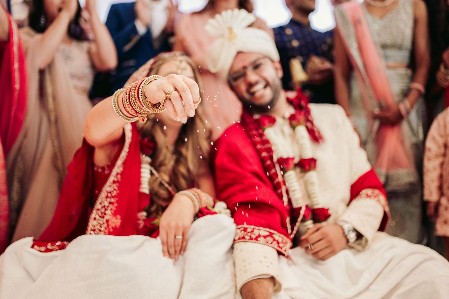 A joyful moment shared during a traditional Indian wedding ceremony with the couple wearing red and white attire.