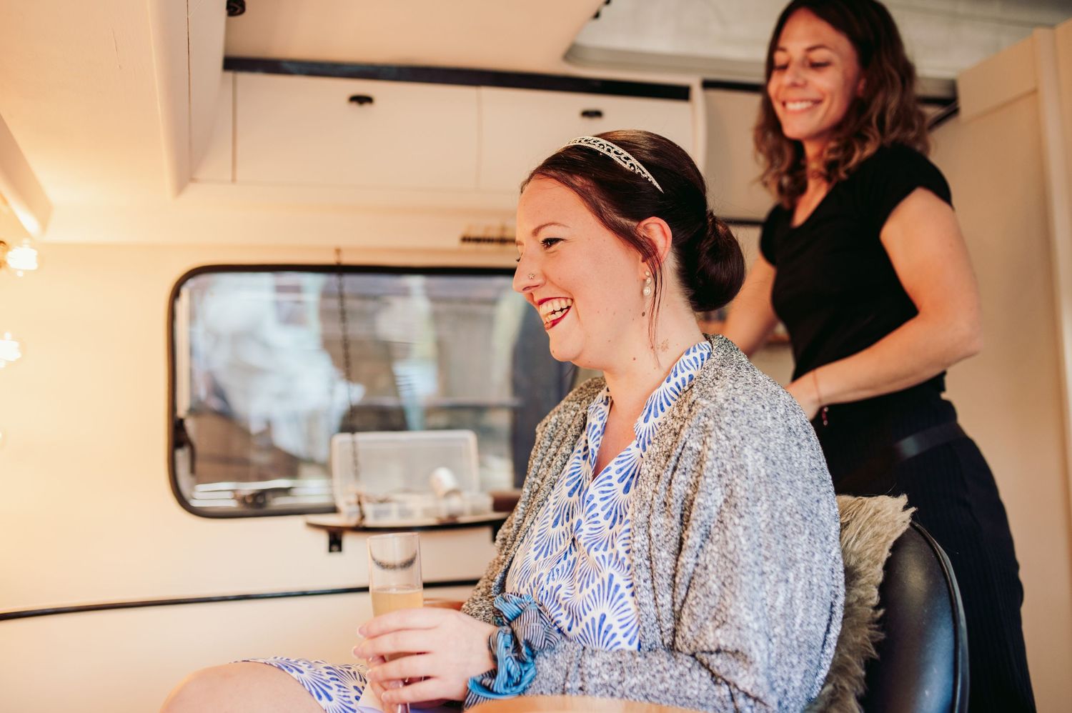 A joyful moment between friends is shared while getting ready inside a sunlit trailer.Spiez switzerland destination wedding