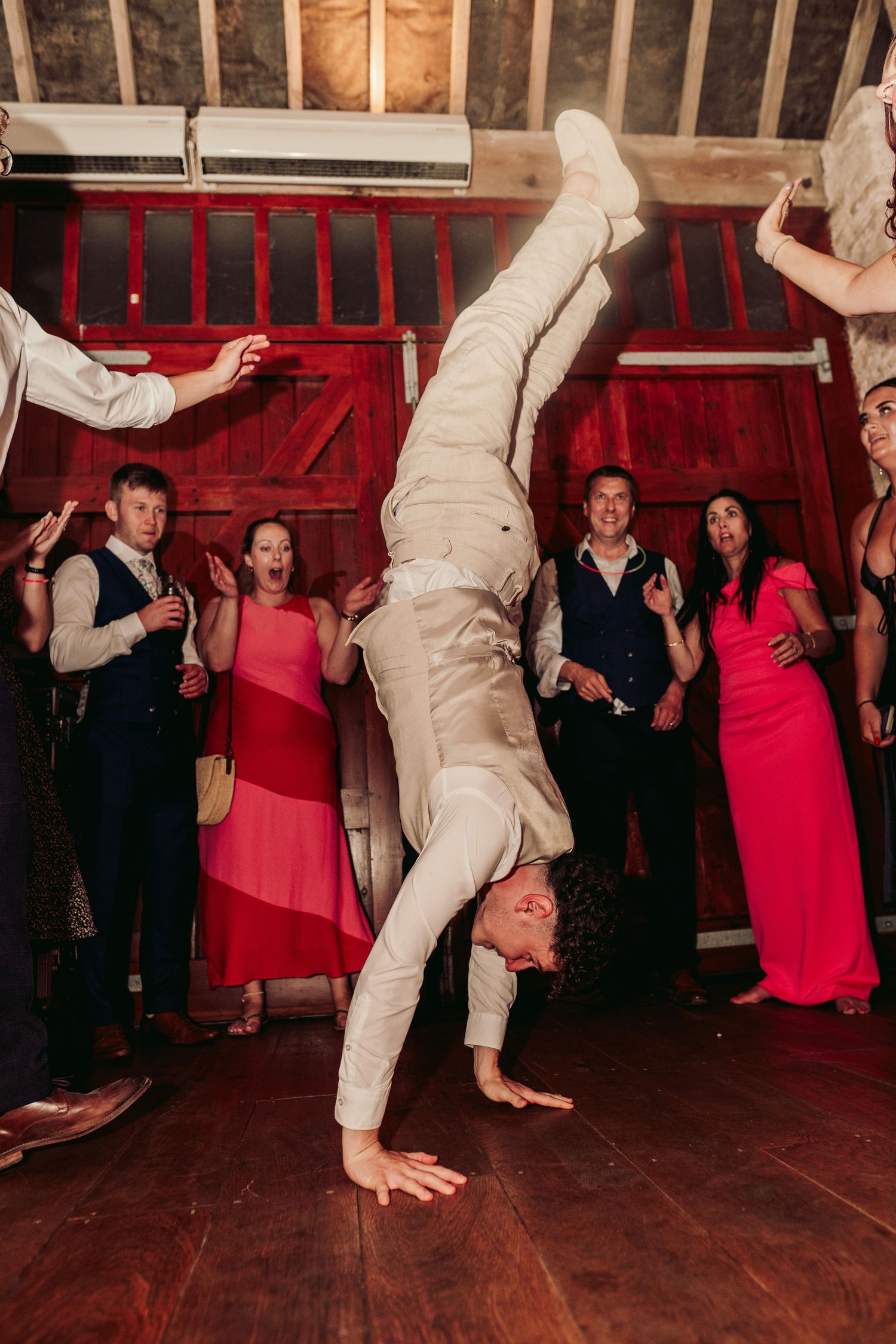 Wedding guests dancing energetically on a rustic wooden floor with red barn walls.