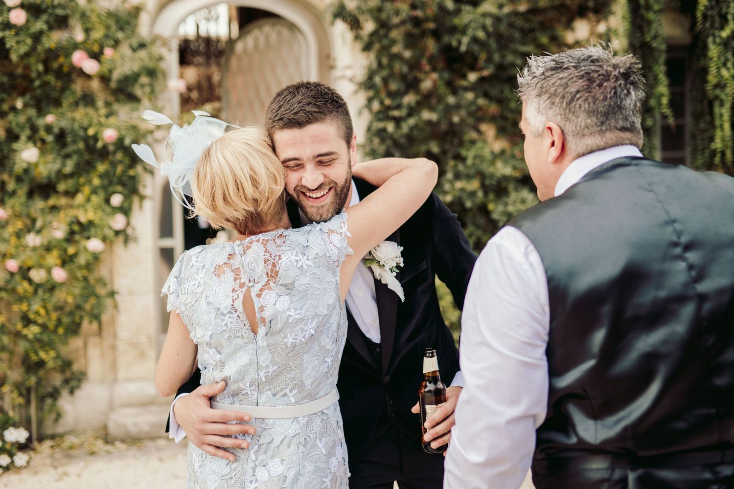 Wedding party shares joyful embraces in garden setting.