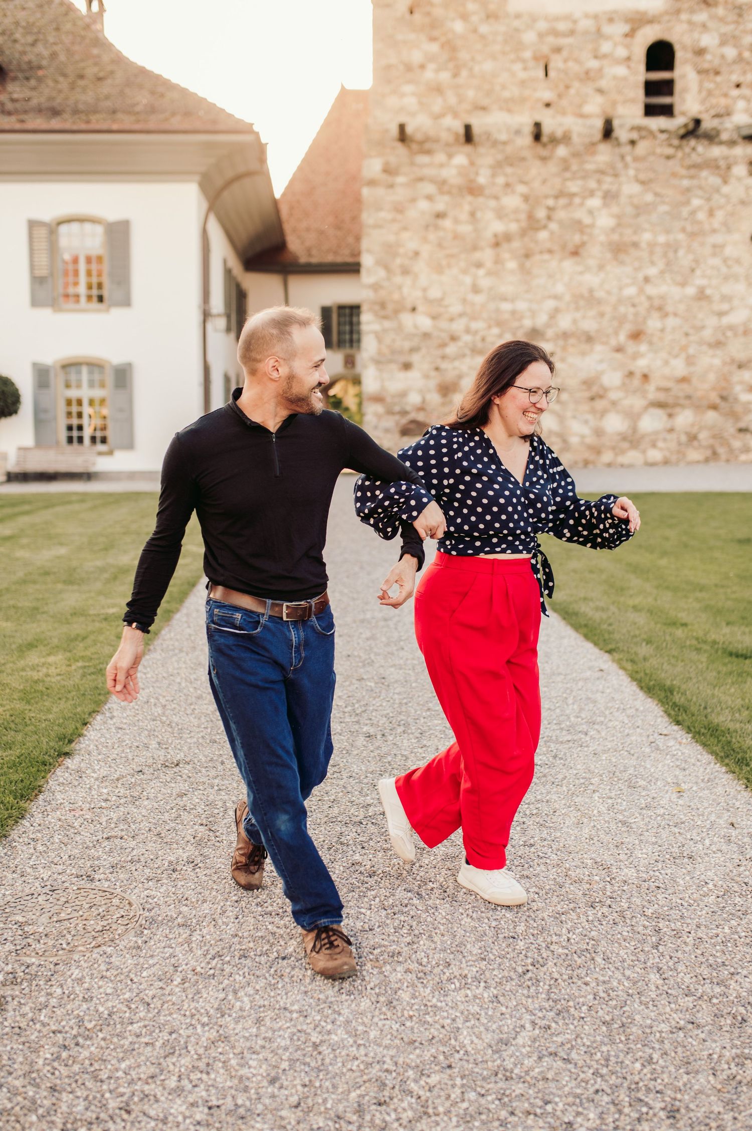 A couple dances joyfully together on a gravel path outside a historic stone castle building with white trim.Spiez switzerland destination