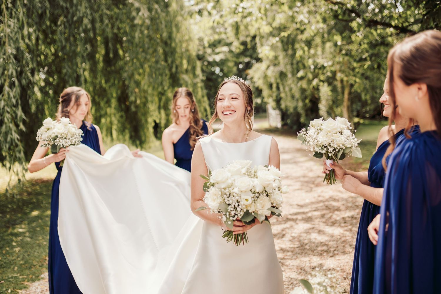 A joyful outdoor wedding celebration with people in navy and white attire gathered in a sunlit garden setting.