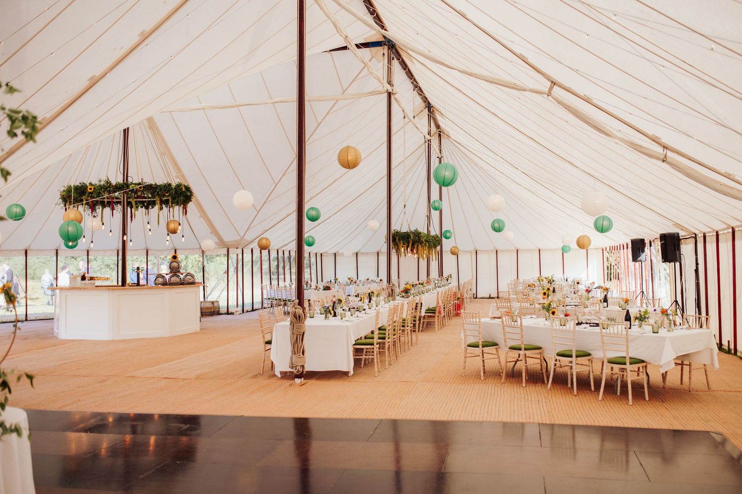 Interior of an elegant white wedding tent with tables set for reception and hanging green paper lanterns.
