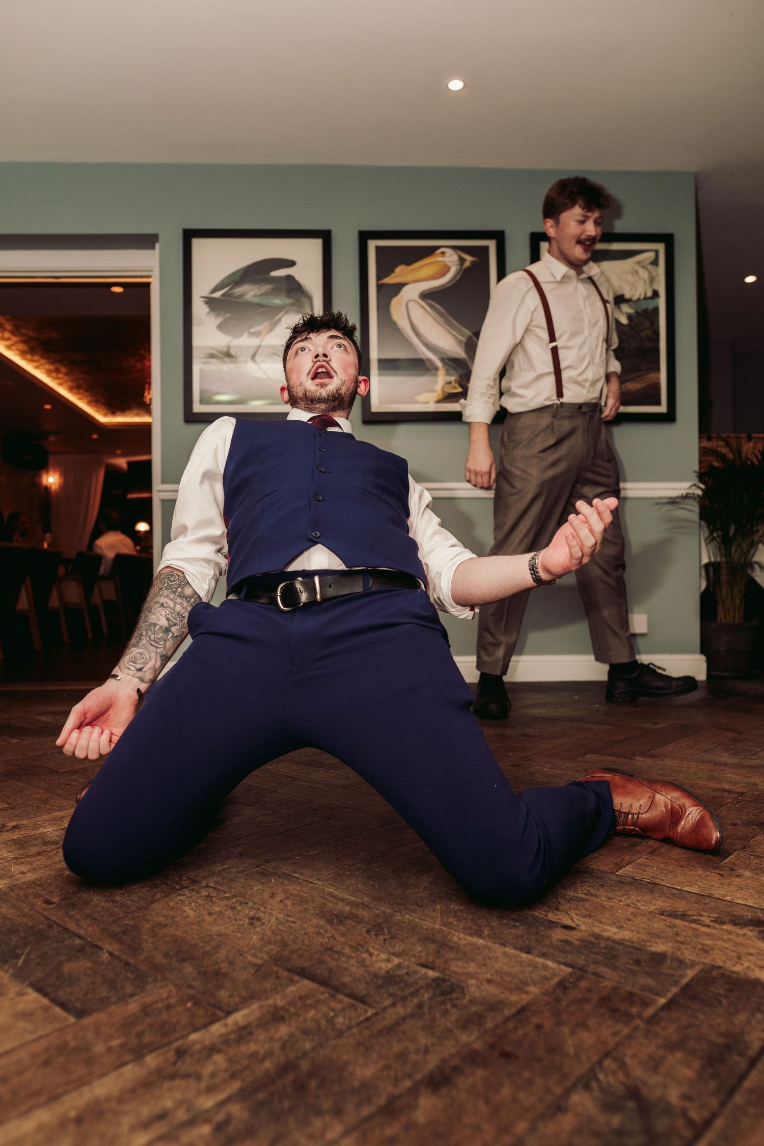 Two guests in vintage attire dancing playfully on a wooden floor with bird artwork in the background.