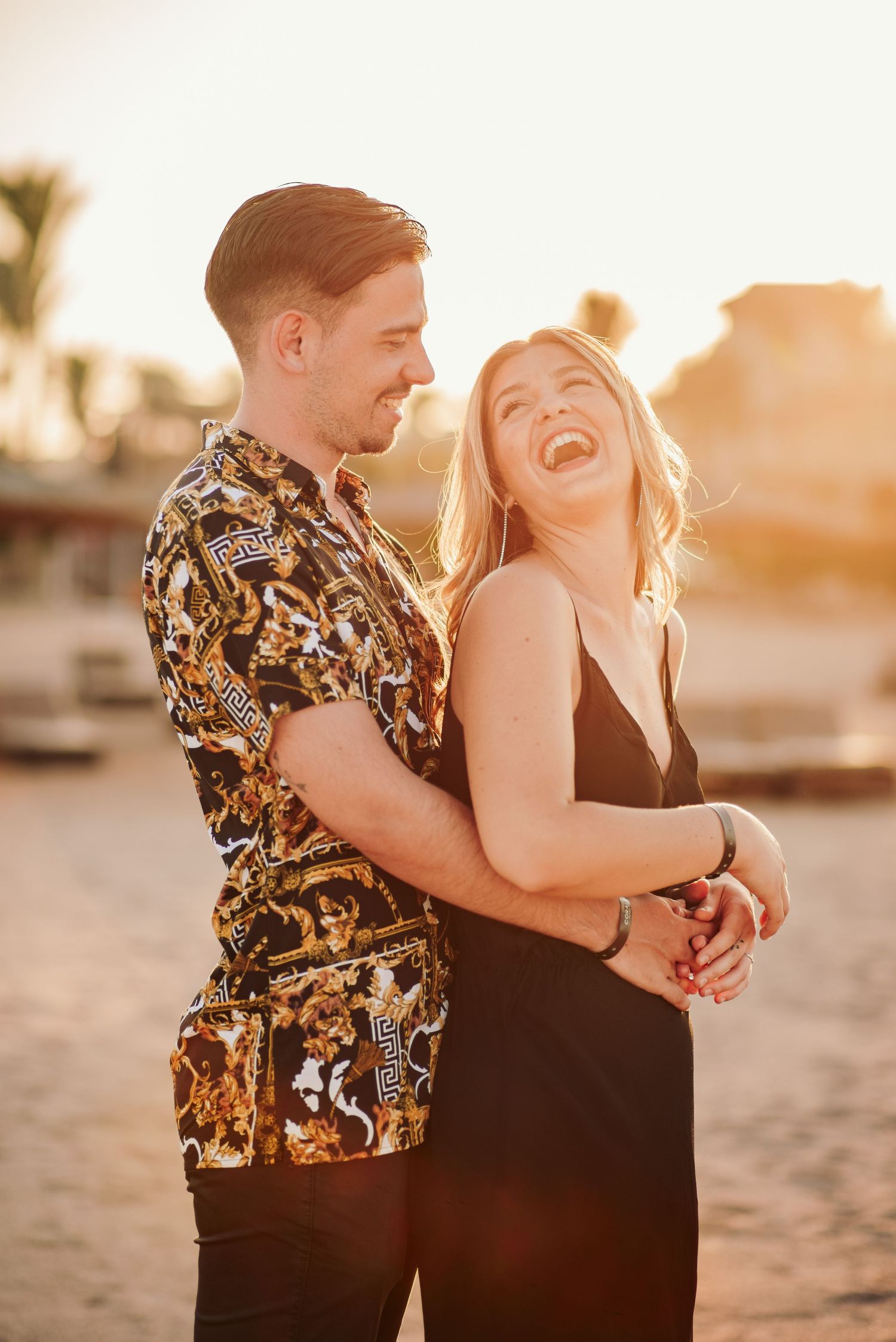 A couple shares a joyful moment at sunset near a marina.
