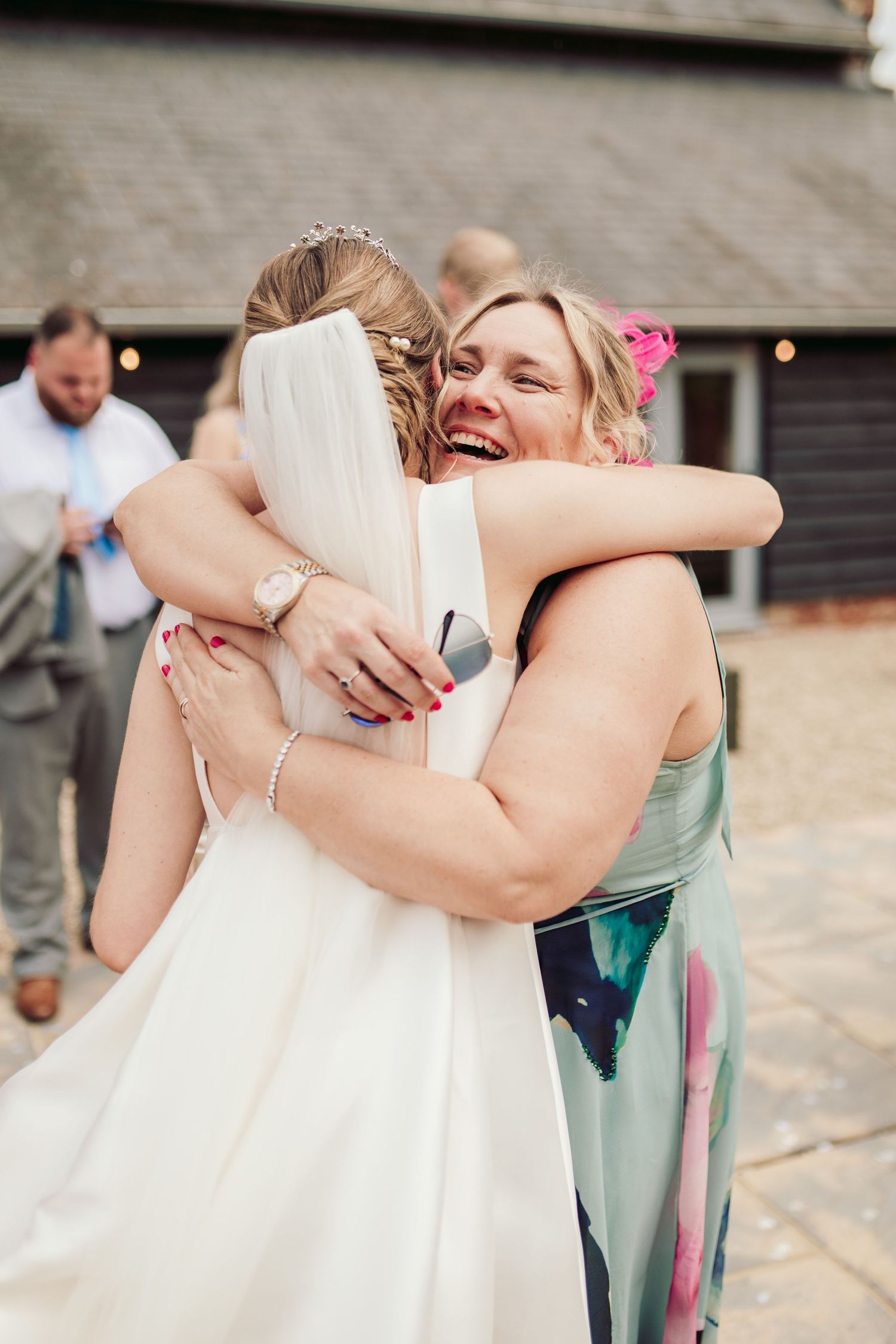 Two people share an emotional embrace at a wedding celebration while wearing formal attire.
