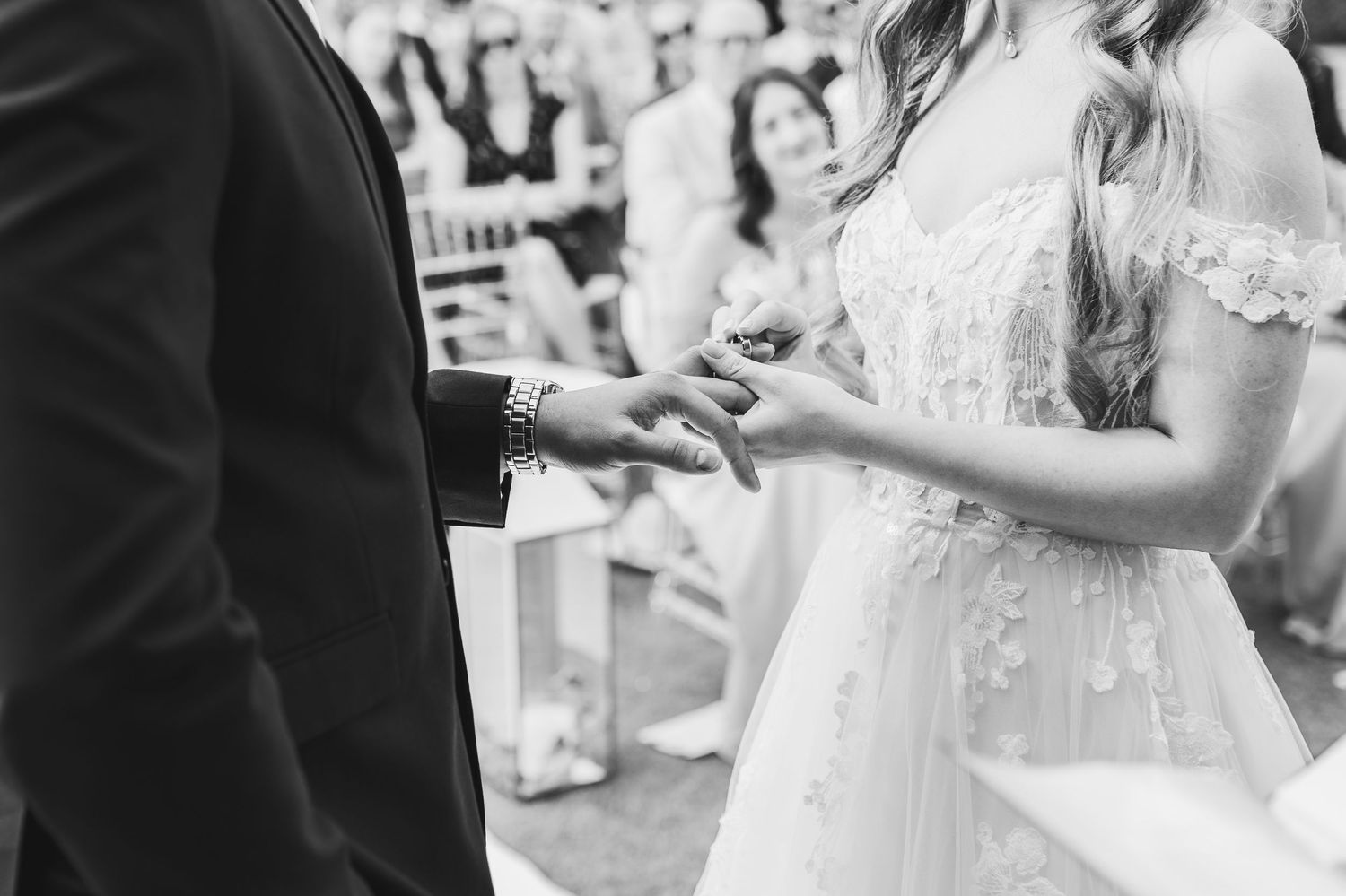 Black and white photo of a wedding ceremony showing hands exchanging rings during an intimate moment.