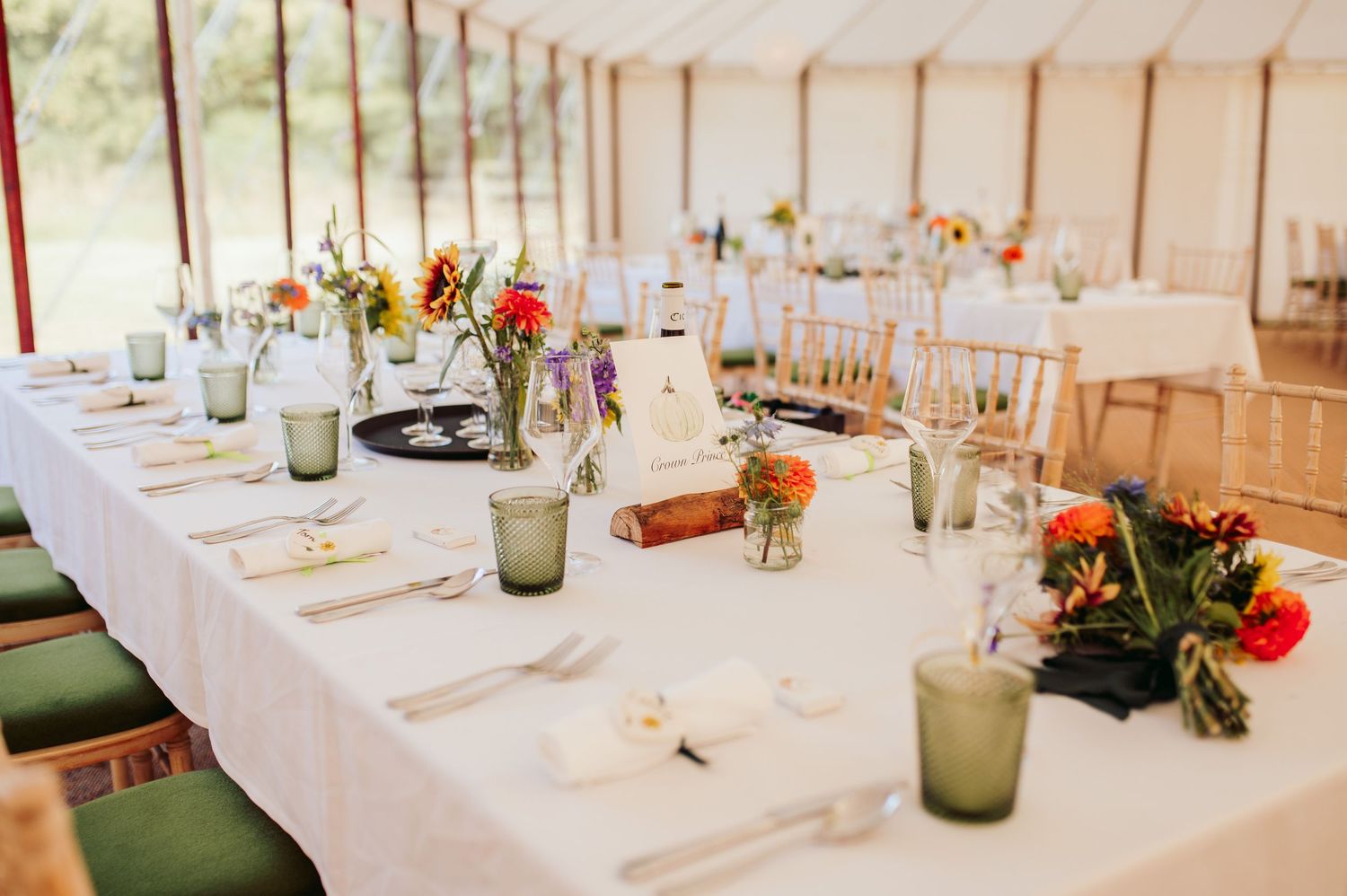 Wedding reception table decorated with white linens, green glassware and colorful floral centerpieces.