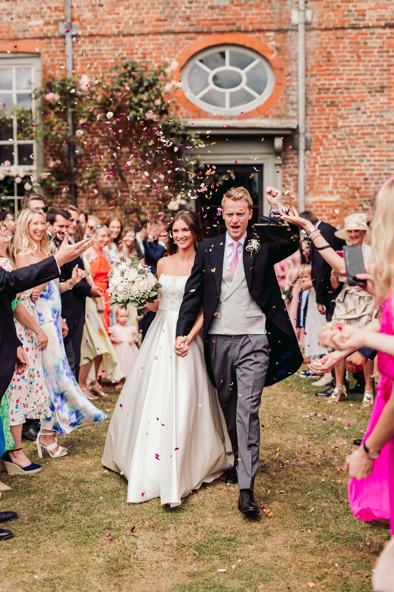 Wedding guests tossing confetti outside a historic brick building during a joyful celebration.