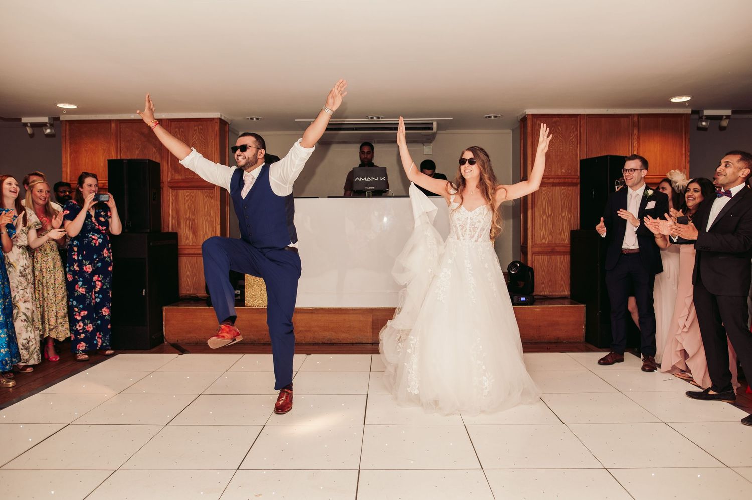 Elegant wedding couple dancing with raised arms on white tiled dance floor while guests applaud at reception.