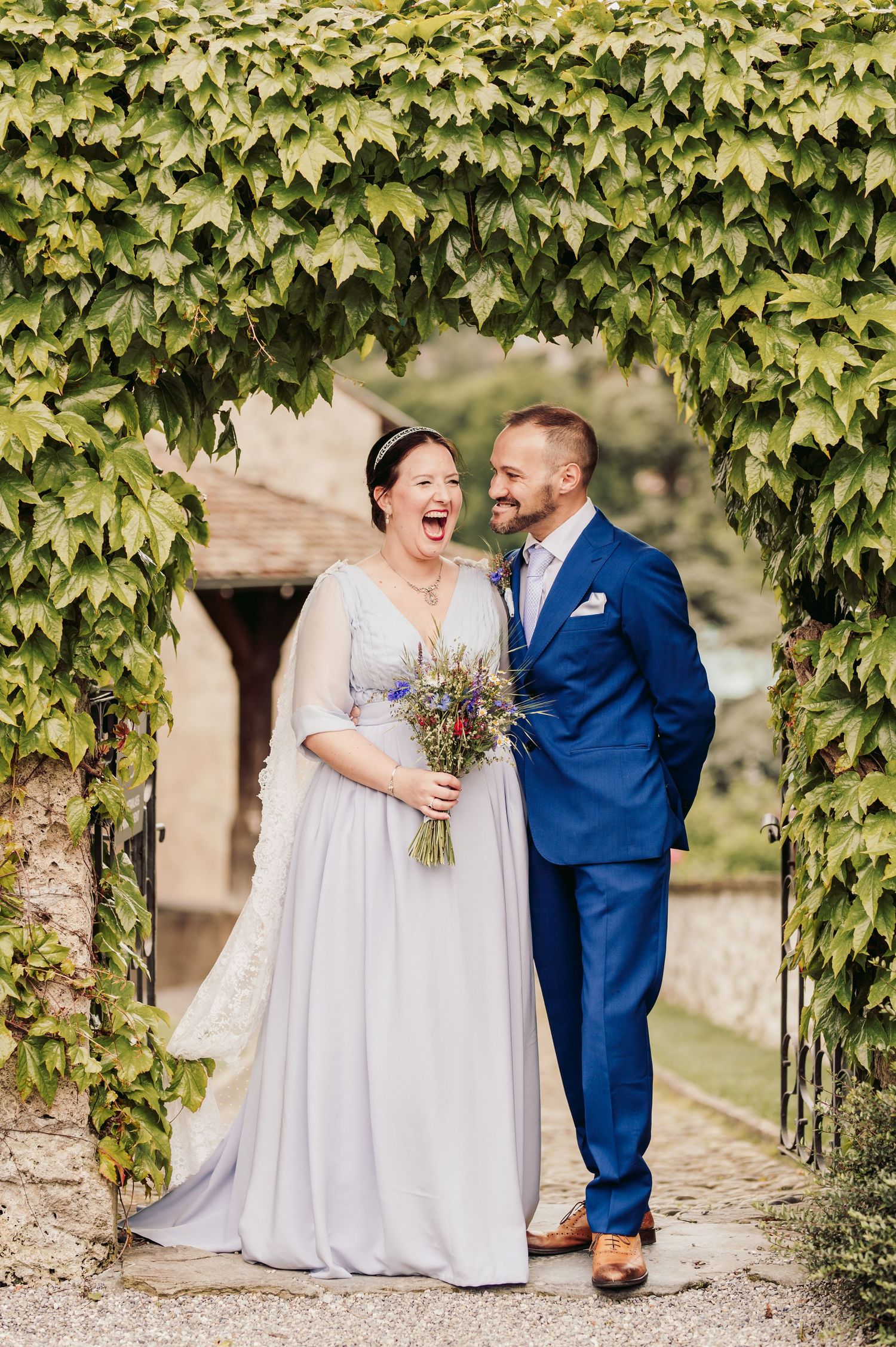A joyful wedding couple shares a candid moment under a natural ivy archway at a rustic outdoor venue. Spiez switzerland destination wedding