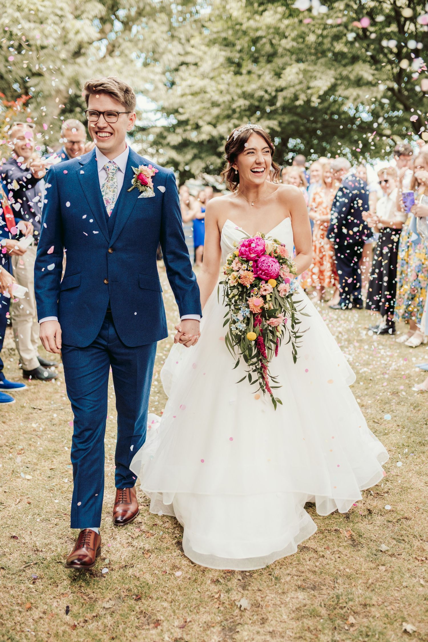 Joyful wedding celebration with confetti shower and colorful bouquet outdoors.