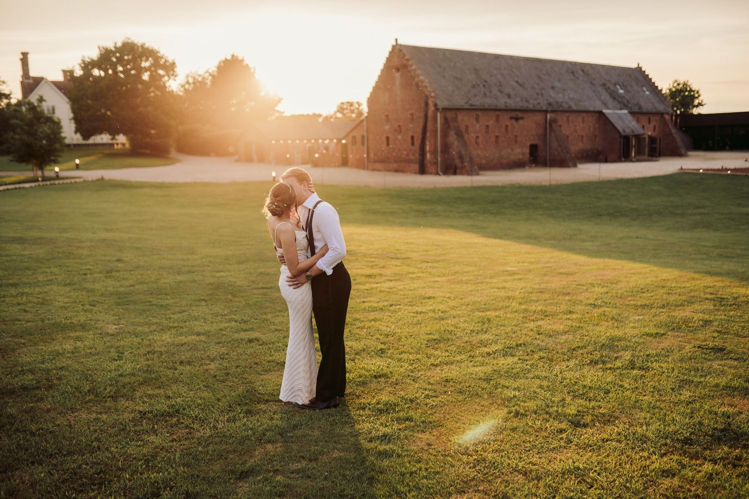 A couple embraces in a golden sunlit field at sunset while sharing a romantic moment.