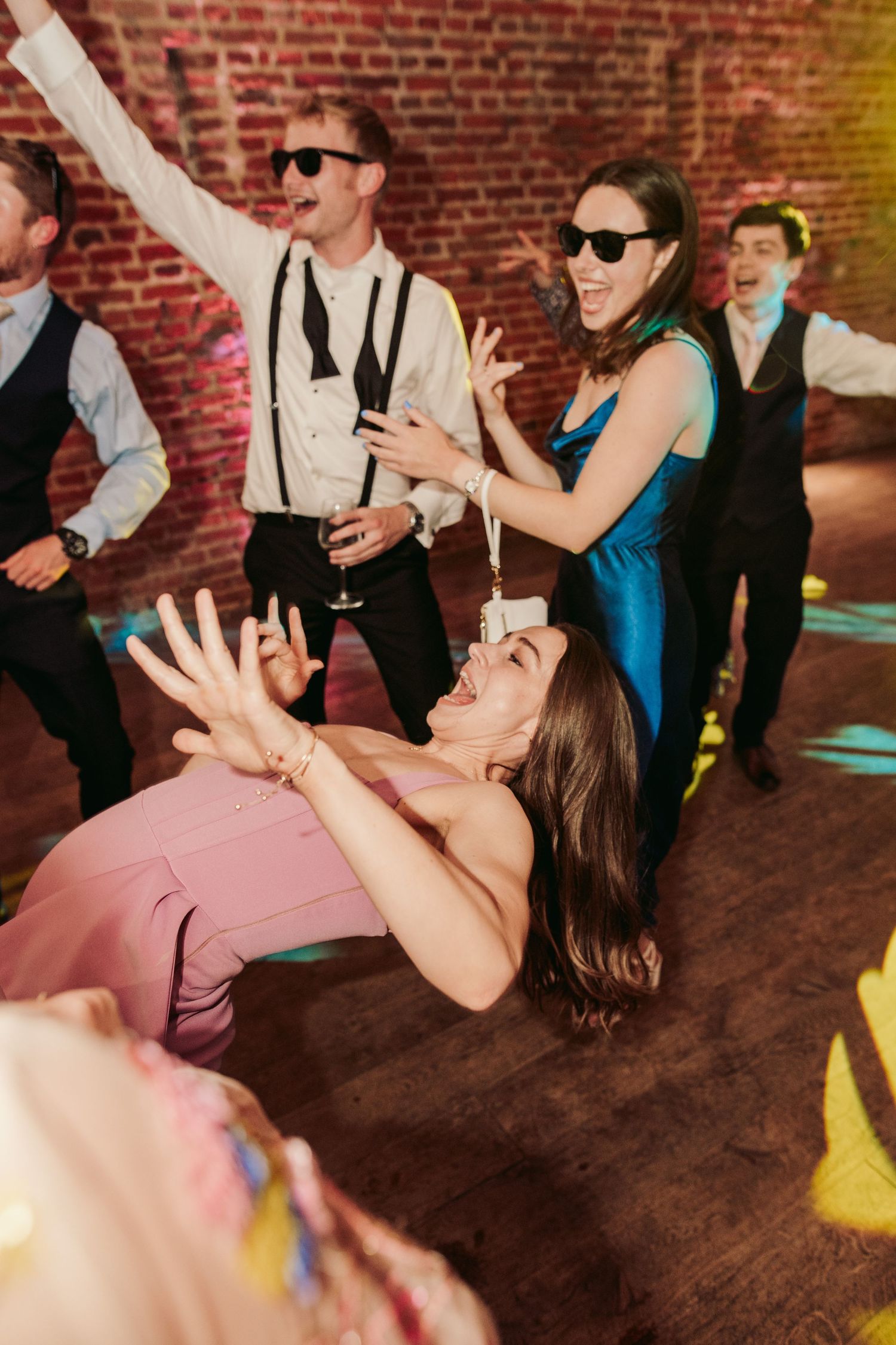 Party guests dancing and having fun at a wedding reception with brick walls and colorful lighting.
