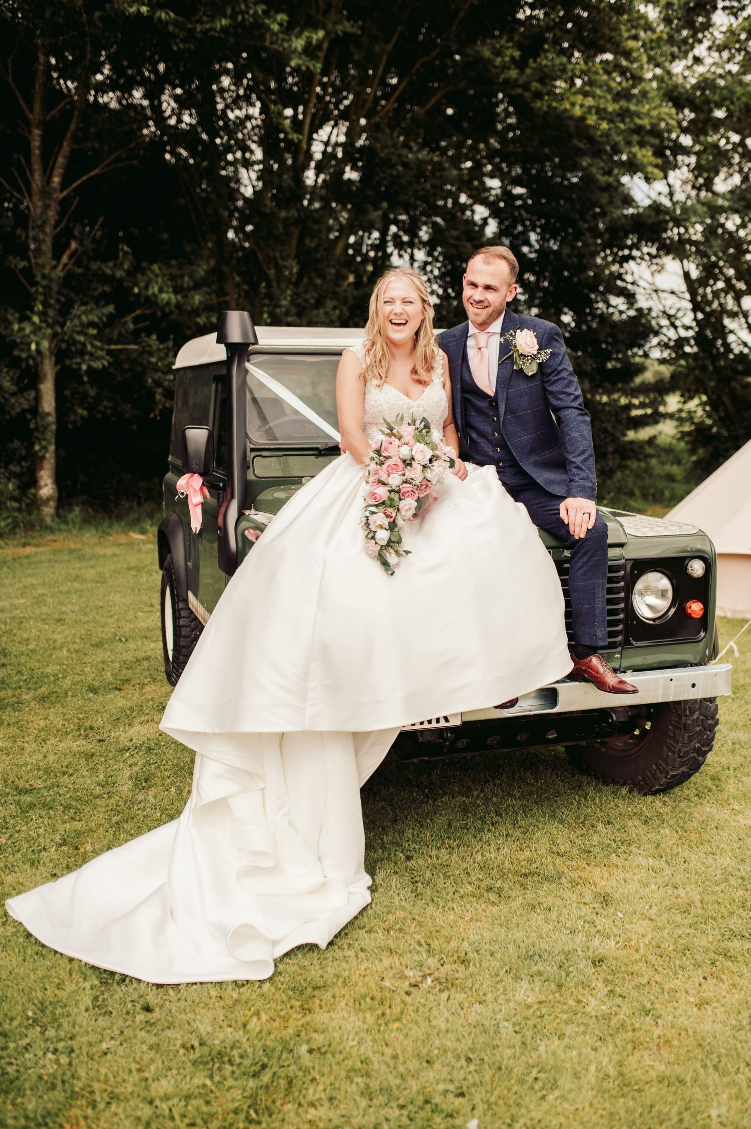 Wedding couple poses with a vintage white car on grassy lawn.